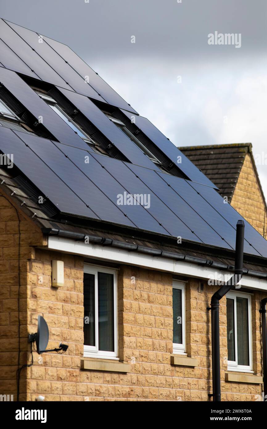 L'énergie solaire joue un rôle limité dans la production d'électricité au Royaume-Uni. Il y avait peu d'installations jusqu'en 2010, lorsque le gouvernement britannique a imposé des subventions sous la forme d'un tarif de rachat (FIT), payé par tous les consommateurs d'électricité. Au cours des années suivantes, le coût des panneaux photovoltaïques (PV) a baissé et les taux D'AJUSTEMENT pour les nouvelles installations ont été réduits progressivement jusqu'à ce que le régime ferme aux nouvelles applications en 2019. En 2023, plus de 14,4 gigawatts (GW) avaient été installés, dont un tiers solaire sur les toits. Maisons et maisons à Queensbury, West Yorkshire, Royaume-Uni avec des panneaux solaires par une journée ensoleillée. Banque D'Images