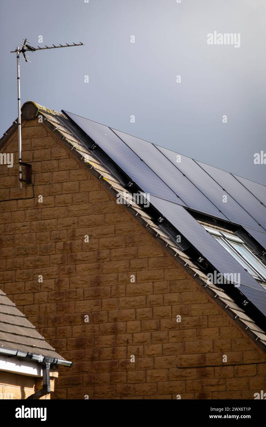 L'énergie solaire joue un rôle limité dans la production d'électricité au Royaume-Uni. Il y avait peu d'installations jusqu'en 2010, lorsque le gouvernement britannique a imposé des subventions sous la forme d'un tarif de rachat (FIT), payé par tous les consommateurs d'électricité. Au cours des années suivantes, le coût des panneaux photovoltaïques (PV) a baissé et les taux D'AJUSTEMENT pour les nouvelles installations ont été réduits progressivement jusqu'à ce que le régime ferme aux nouvelles applications en 2019. En 2023, plus de 14,4 gigawatts (GW) avaient été installés, dont un tiers solaire sur les toits. Maisons et maisons à Queensbury, West Yorkshire, Royaume-Uni avec des panneaux solaires par une journée ensoleillée. Banque D'Images