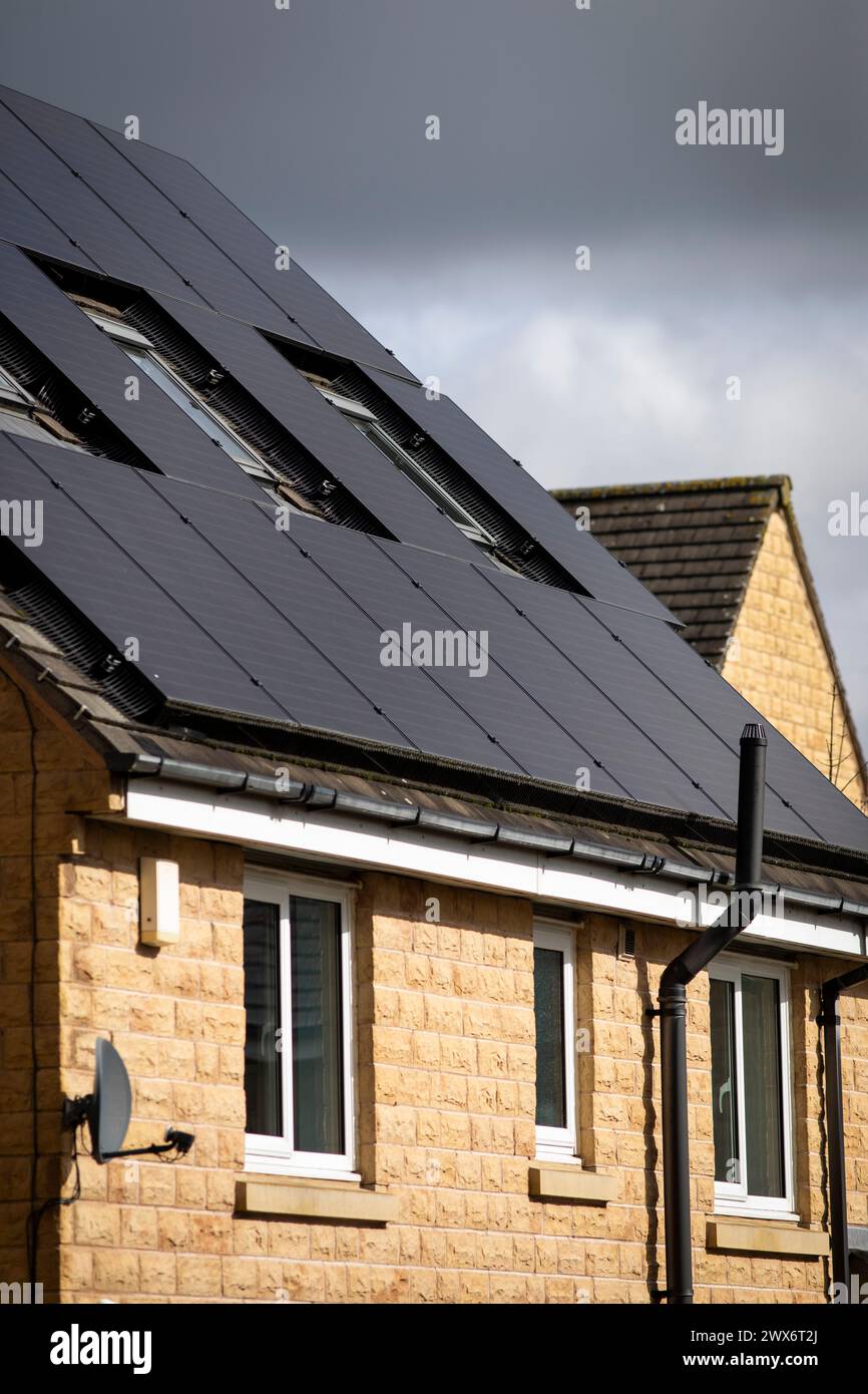 L'énergie solaire joue un rôle limité dans la production d'électricité au Royaume-Uni. Il y avait peu d'installations jusqu'en 2010, lorsque le gouvernement britannique a imposé des subventions sous la forme d'un tarif de rachat (FIT), payé par tous les consommateurs d'électricité. Au cours des années suivantes, le coût des panneaux photovoltaïques (PV) a baissé et les taux D'AJUSTEMENT pour les nouvelles installations ont été réduits progressivement jusqu'à ce que le régime ferme aux nouvelles applications en 2019. En 2023, plus de 14,4 gigawatts (GW) avaient été installés, dont un tiers solaire sur les toits. Maisons et maisons à Queensbury, West Yorkshire, Royaume-Uni avec des panneaux solaires par une journée ensoleillée. Banque D'Images