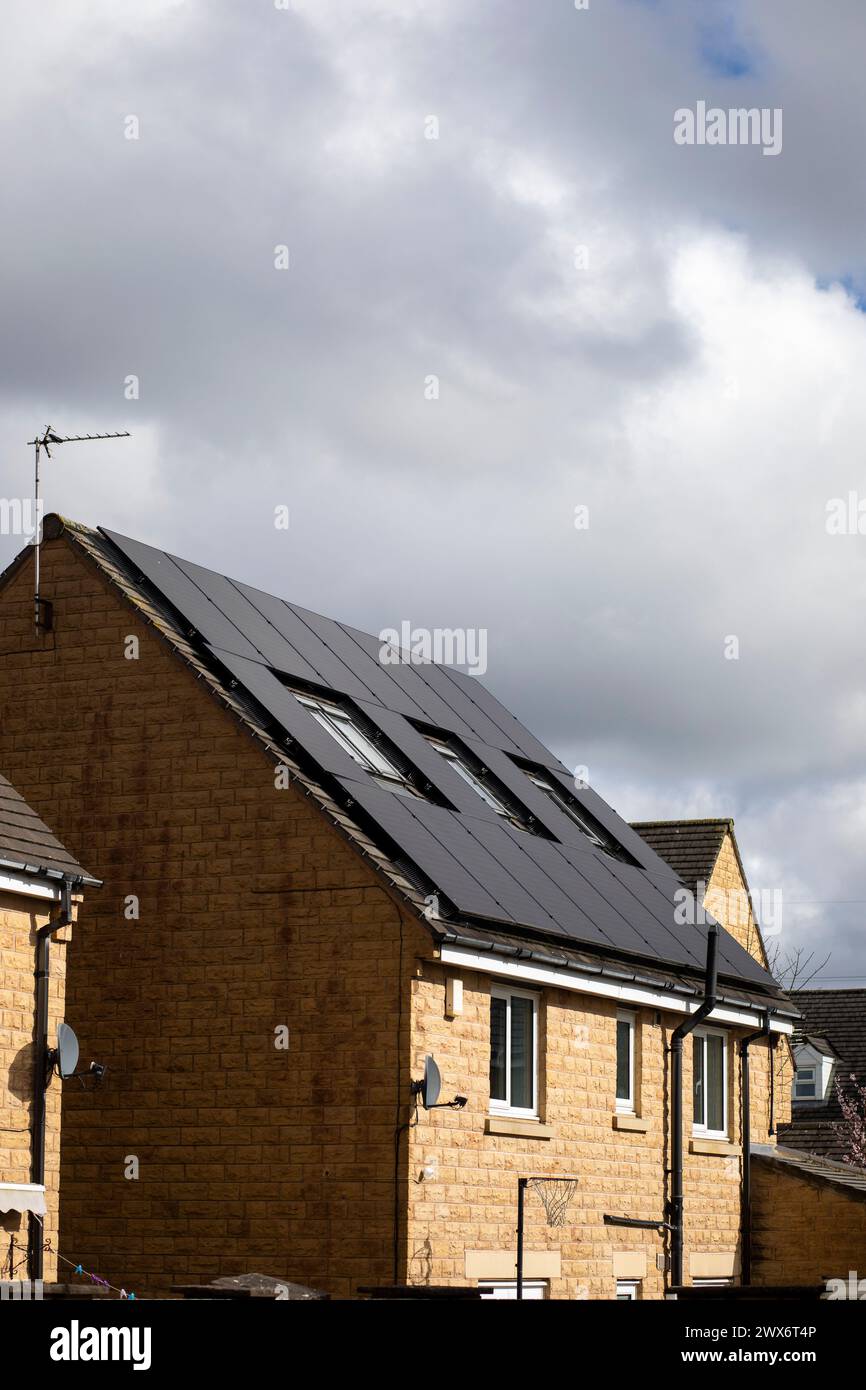 L'énergie solaire joue un rôle limité dans la production d'électricité au Royaume-Uni. Il y avait peu d'installations jusqu'en 2010, lorsque le gouvernement britannique a imposé des subventions sous la forme d'un tarif de rachat (FIT), payé par tous les consommateurs d'électricité. Au cours des années suivantes, le coût des panneaux photovoltaïques (PV) a baissé et les taux D'AJUSTEMENT pour les nouvelles installations ont été réduits progressivement jusqu'à ce que le régime ferme aux nouvelles applications en 2019. En 2023, plus de 14,4 gigawatts (GW) avaient été installés, dont un tiers solaire sur les toits. Maisons et maisons à Queensbury, West Yorkshire, Royaume-Uni avec des panneaux solaires par une journée ensoleillée. Banque D'Images