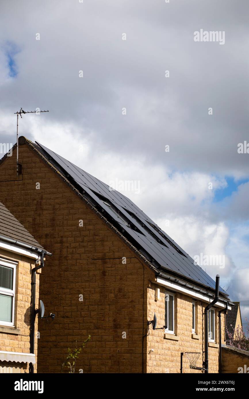 L'énergie solaire joue un rôle limité dans la production d'électricité au Royaume-Uni. Il y avait peu d'installations jusqu'en 2010, lorsque le gouvernement britannique a imposé des subventions sous la forme d'un tarif de rachat (FIT), payé par tous les consommateurs d'électricité. Au cours des années suivantes, le coût des panneaux photovoltaïques (PV) a baissé et les taux D'AJUSTEMENT pour les nouvelles installations ont été réduits progressivement jusqu'à ce que le régime ferme aux nouvelles applications en 2019. En 2023, plus de 14,4 gigawatts (GW) avaient été installés, dont un tiers solaire sur les toits. Maisons et maisons à Queensbury, West Yorkshire, Royaume-Uni avec des panneaux solaires par une journée ensoleillée. Banque D'Images