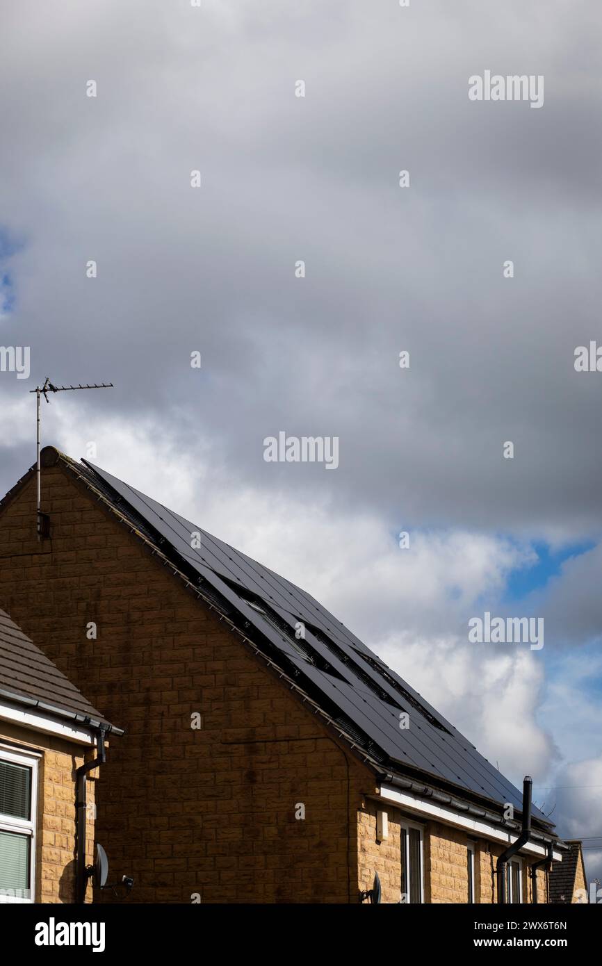 L'énergie solaire joue un rôle limité dans la production d'électricité au Royaume-Uni. Il y avait peu d'installations jusqu'en 2010, lorsque le gouvernement britannique a imposé des subventions sous la forme d'un tarif de rachat (FIT), payé par tous les consommateurs d'électricité. Au cours des années suivantes, le coût des panneaux photovoltaïques (PV) a baissé et les taux D'AJUSTEMENT pour les nouvelles installations ont été réduits progressivement jusqu'à ce que le régime ferme aux nouvelles applications en 2019. En 2023, plus de 14,4 gigawatts (GW) avaient été installés, dont un tiers solaire sur les toits. Maisons et maisons à Queensbury, West Yorkshire, Royaume-Uni avec des panneaux solaires par une journée ensoleillée. Banque D'Images