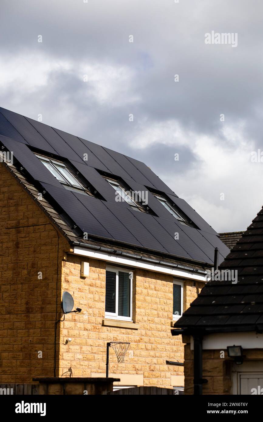 L'énergie solaire joue un rôle limité dans la production d'électricité au Royaume-Uni. Il y avait peu d'installations jusqu'en 2010, lorsque le gouvernement britannique a imposé des subventions sous la forme d'un tarif de rachat (FIT), payé par tous les consommateurs d'électricité. Au cours des années suivantes, le coût des panneaux photovoltaïques (PV) a baissé et les taux D'AJUSTEMENT pour les nouvelles installations ont été réduits progressivement jusqu'à ce que le régime ferme aux nouvelles applications en 2019. En 2023, plus de 14,4 gigawatts (GW) avaient été installés, dont un tiers solaire sur les toits. Maisons et maisons à Queensbury, West Yorkshire, Royaume-Uni avec des panneaux solaires par une journée ensoleillée. Banque D'Images