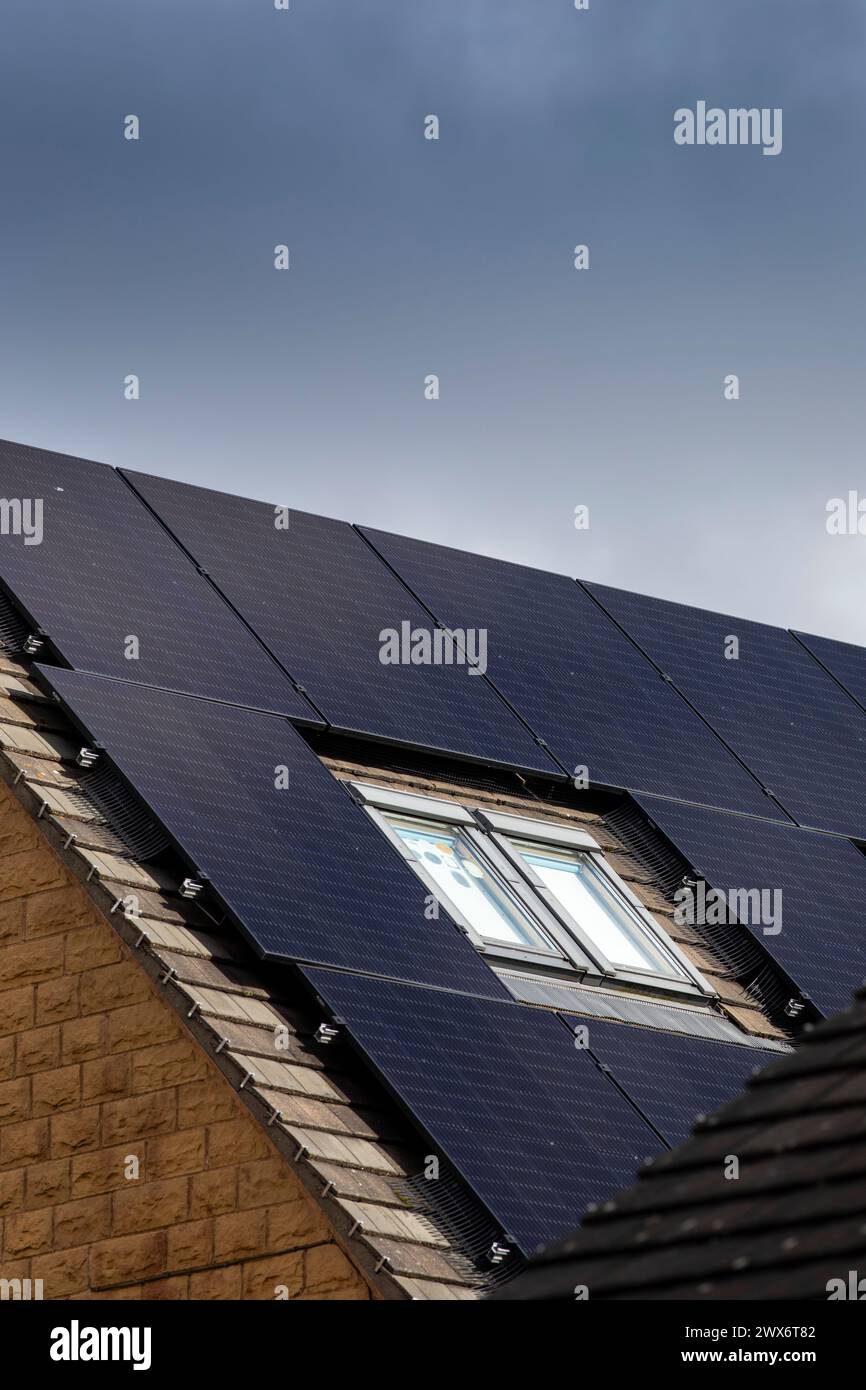 L'énergie solaire joue un rôle limité dans la production d'électricité au Royaume-Uni. Il y avait peu d'installations jusqu'en 2010, lorsque le gouvernement britannique a imposé des subventions sous la forme d'un tarif de rachat (FIT), payé par tous les consommateurs d'électricité. Au cours des années suivantes, le coût des panneaux photovoltaïques (PV) a baissé et les taux D'AJUSTEMENT pour les nouvelles installations ont été réduits progressivement jusqu'à ce que le régime ferme aux nouvelles applications en 2019. En 2023, plus de 14,4 gigawatts (GW) avaient été installés, dont un tiers solaire sur les toits. Maisons et maisons à Queensbury, West Yorkshire, Royaume-Uni avec des panneaux solaires par une journée ensoleillée. Banque D'Images