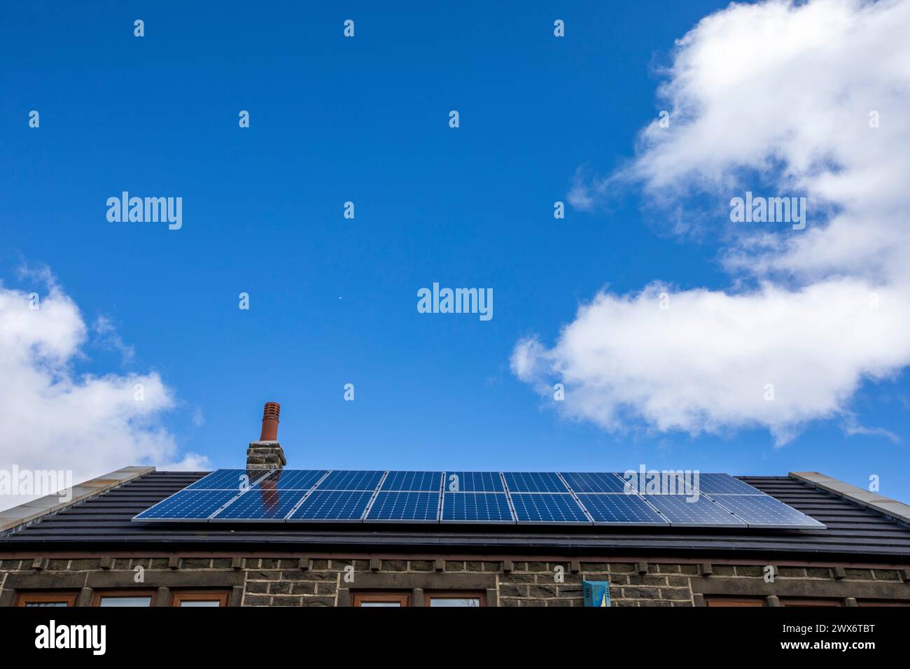 L'énergie solaire joue un rôle limité dans la production d'électricité au Royaume-Uni. Il y avait peu d'installations jusqu'en 2010, lorsque le gouvernement britannique a imposé des subventions sous la forme d'un tarif de rachat (FIT), payé par tous les consommateurs d'électricité. Au cours des années suivantes, le coût des panneaux photovoltaïques (PV) a baissé et les taux D'AJUSTEMENT pour les nouvelles installations ont été réduits progressivement jusqu'à ce que le régime ferme aux nouvelles applications en 2019. En 2023, plus de 14,4 gigawatts (GW) avaient été installés, dont un tiers solaire sur les toits. Maisons et maisons à Queensbury, West Yorkshire, Royaume-Uni avec des panneaux solaires par une journée ensoleillée. Banque D'Images