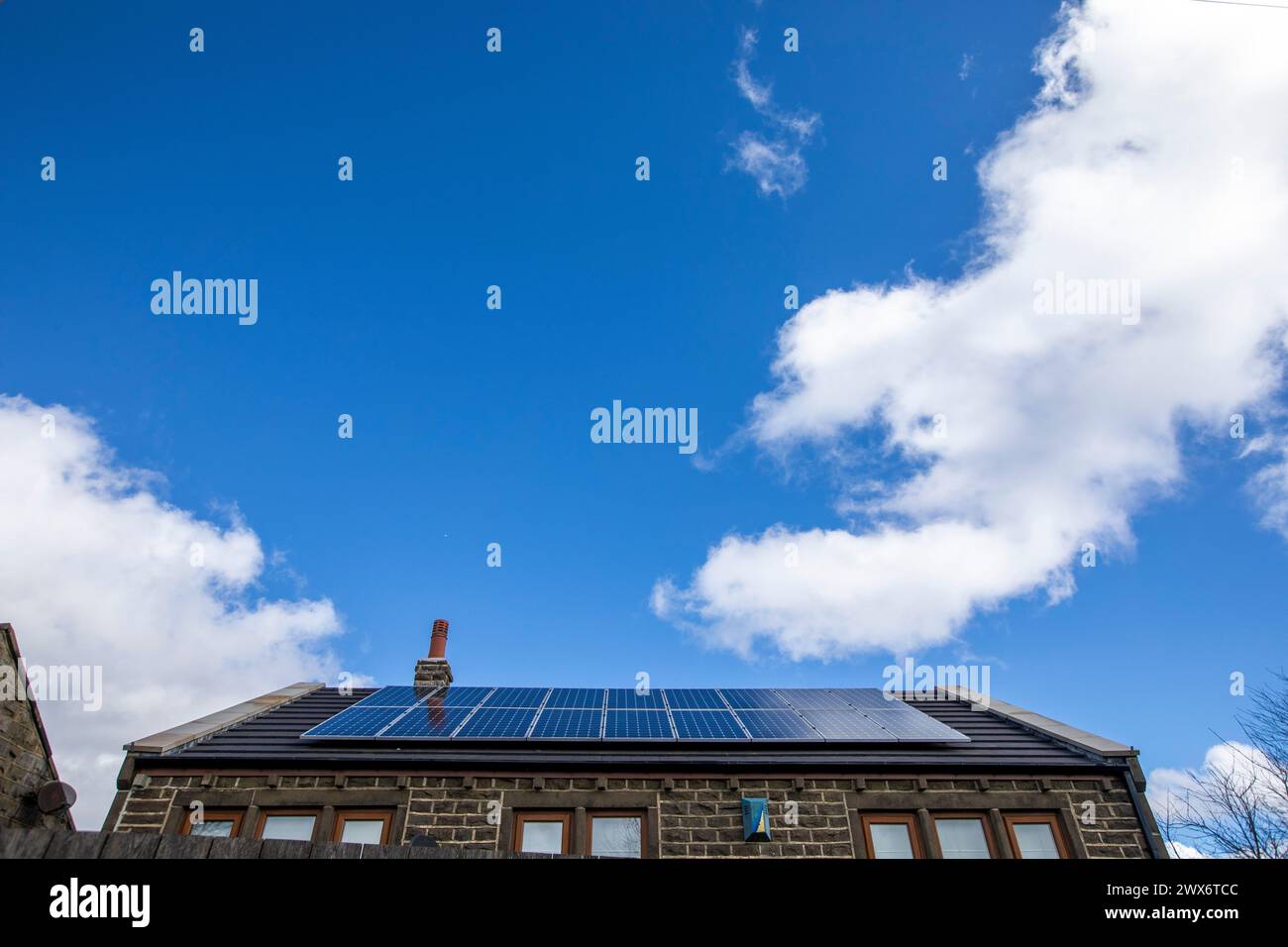 L'énergie solaire joue un rôle limité dans la production d'électricité au Royaume-Uni. Il y avait peu d'installations jusqu'en 2010, lorsque le gouvernement britannique a imposé des subventions sous la forme d'un tarif de rachat (FIT), payé par tous les consommateurs d'électricité. Au cours des années suivantes, le coût des panneaux photovoltaïques (PV) a baissé et les taux D'AJUSTEMENT pour les nouvelles installations ont été réduits progressivement jusqu'à ce que le régime ferme aux nouvelles applications en 2019. En 2023, plus de 14,4 gigawatts (GW) avaient été installés, dont un tiers solaire sur les toits. Maisons et maisons à Queensbury, West Yorkshire, Royaume-Uni avec des panneaux solaires par une journée ensoleillée. Banque D'Images