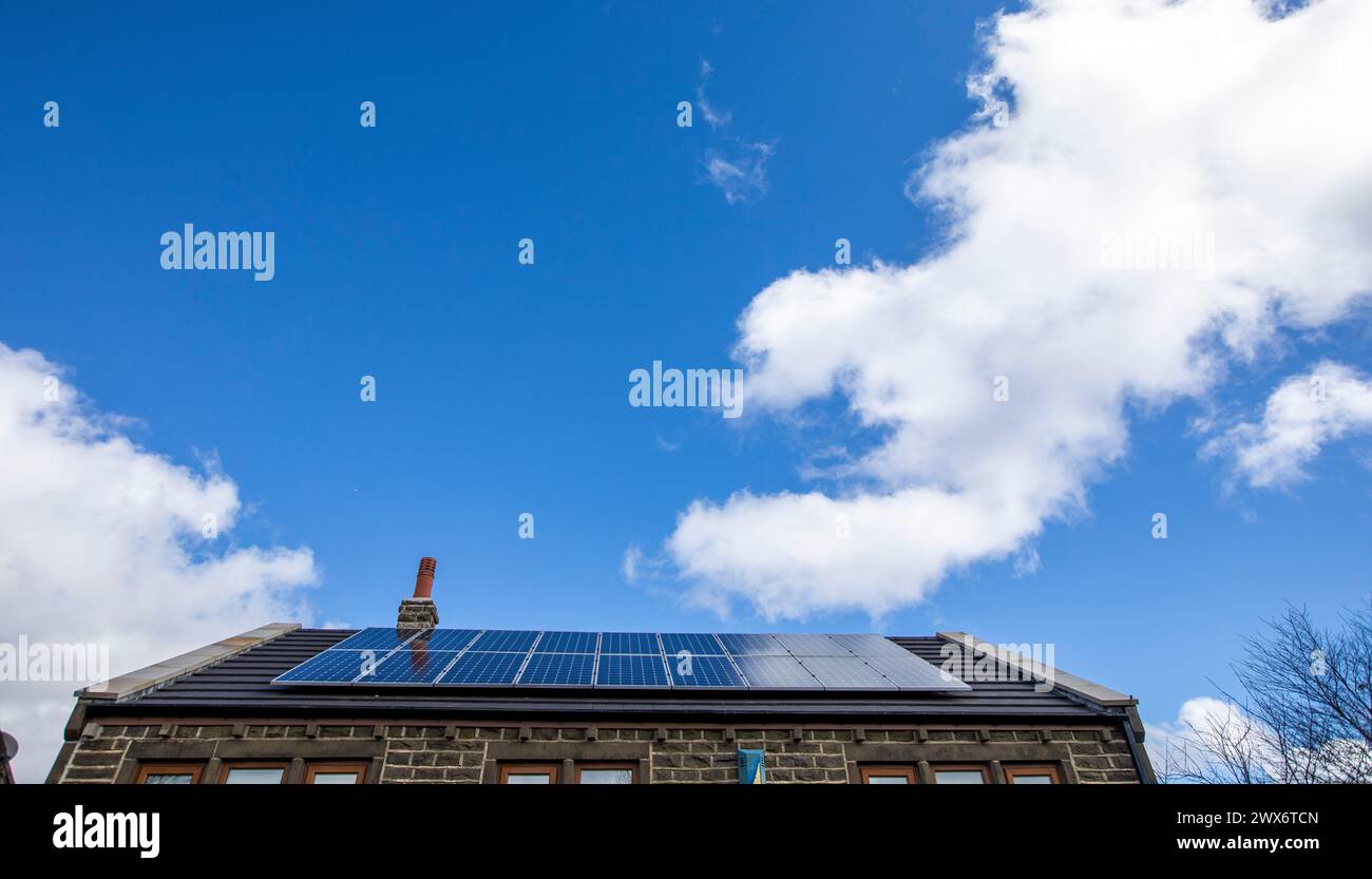 L'énergie solaire joue un rôle limité dans la production d'électricité au Royaume-Uni. Il y avait peu d'installations jusqu'en 2010, lorsque le gouvernement britannique a imposé des subventions sous la forme d'un tarif de rachat (FIT), payé par tous les consommateurs d'électricité. Au cours des années suivantes, le coût des panneaux photovoltaïques (PV) a baissé et les taux D'AJUSTEMENT pour les nouvelles installations ont été réduits progressivement jusqu'à ce que le régime ferme aux nouvelles applications en 2019. En 2023, plus de 14,4 gigawatts (GW) avaient été installés, dont un tiers solaire sur les toits. Maisons et maisons à Queensbury, West Yorkshire, Royaume-Uni avec des panneaux solaires par une journée ensoleillée. Banque D'Images