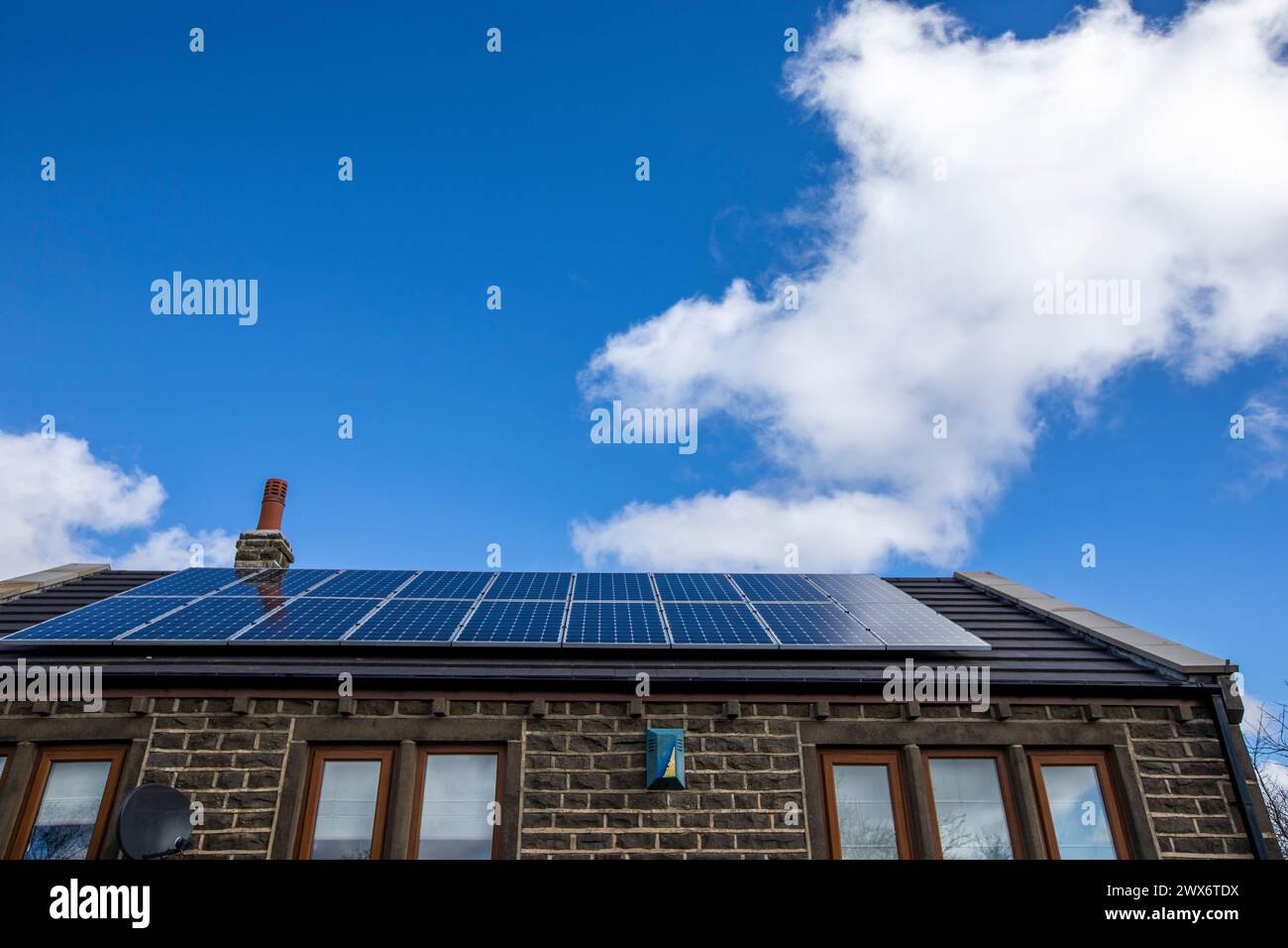 L'énergie solaire joue un rôle limité dans la production d'électricité au Royaume-Uni. Il y avait peu d'installations jusqu'en 2010, lorsque le gouvernement britannique a imposé des subventions sous la forme d'un tarif de rachat (FIT), payé par tous les consommateurs d'électricité. Au cours des années suivantes, le coût des panneaux photovoltaïques (PV) a baissé et les taux D'AJUSTEMENT pour les nouvelles installations ont été réduits progressivement jusqu'à ce que le régime ferme aux nouvelles applications en 2019. En 2023, plus de 14,4 gigawatts (GW) avaient été installés, dont un tiers solaire sur les toits. Maisons et maisons à Queensbury, West Yorkshire, Royaume-Uni avec des panneaux solaires par une journée ensoleillée. Banque D'Images