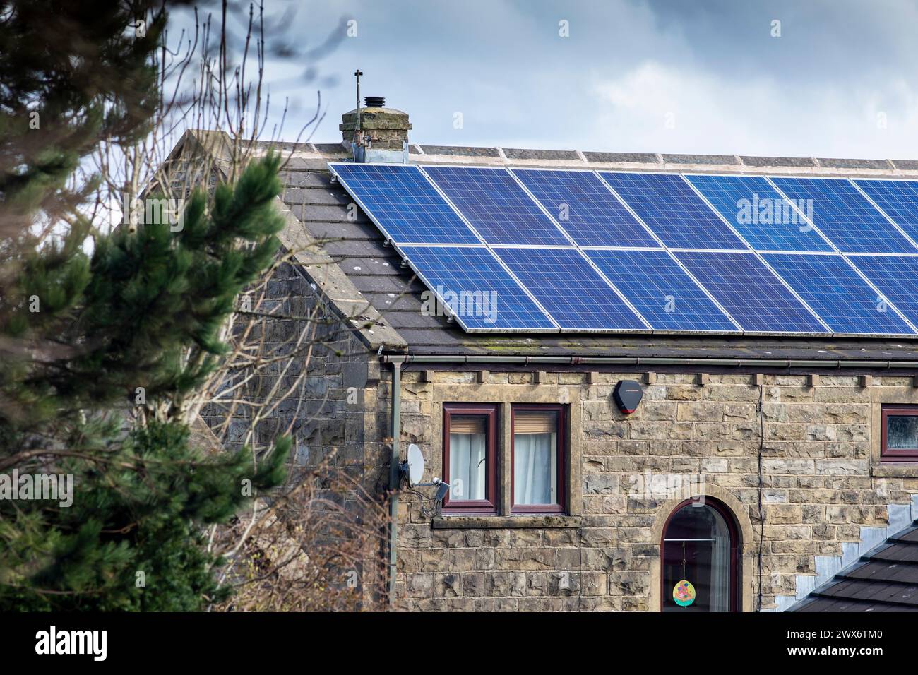L'énergie solaire joue un rôle limité dans la production d'électricité au Royaume-Uni. Il y avait peu d'installations jusqu'en 2010, lorsque le gouvernement britannique a imposé des subventions sous la forme d'un tarif de rachat (FIT), payé par tous les consommateurs d'électricité. Au cours des années suivantes, le coût des panneaux photovoltaïques (PV) a baissé et les taux D'AJUSTEMENT pour les nouvelles installations ont été réduits progressivement jusqu'à ce que le régime ferme aux nouvelles applications en 2019. En 2023, plus de 14,4 gigawatts (GW) avaient été installés, dont un tiers solaire sur les toits. Maisons et maisons à Queensbury, West Yorkshire, Royaume-Uni avec des panneaux solaires par une journée ensoleillée. Banque D'Images