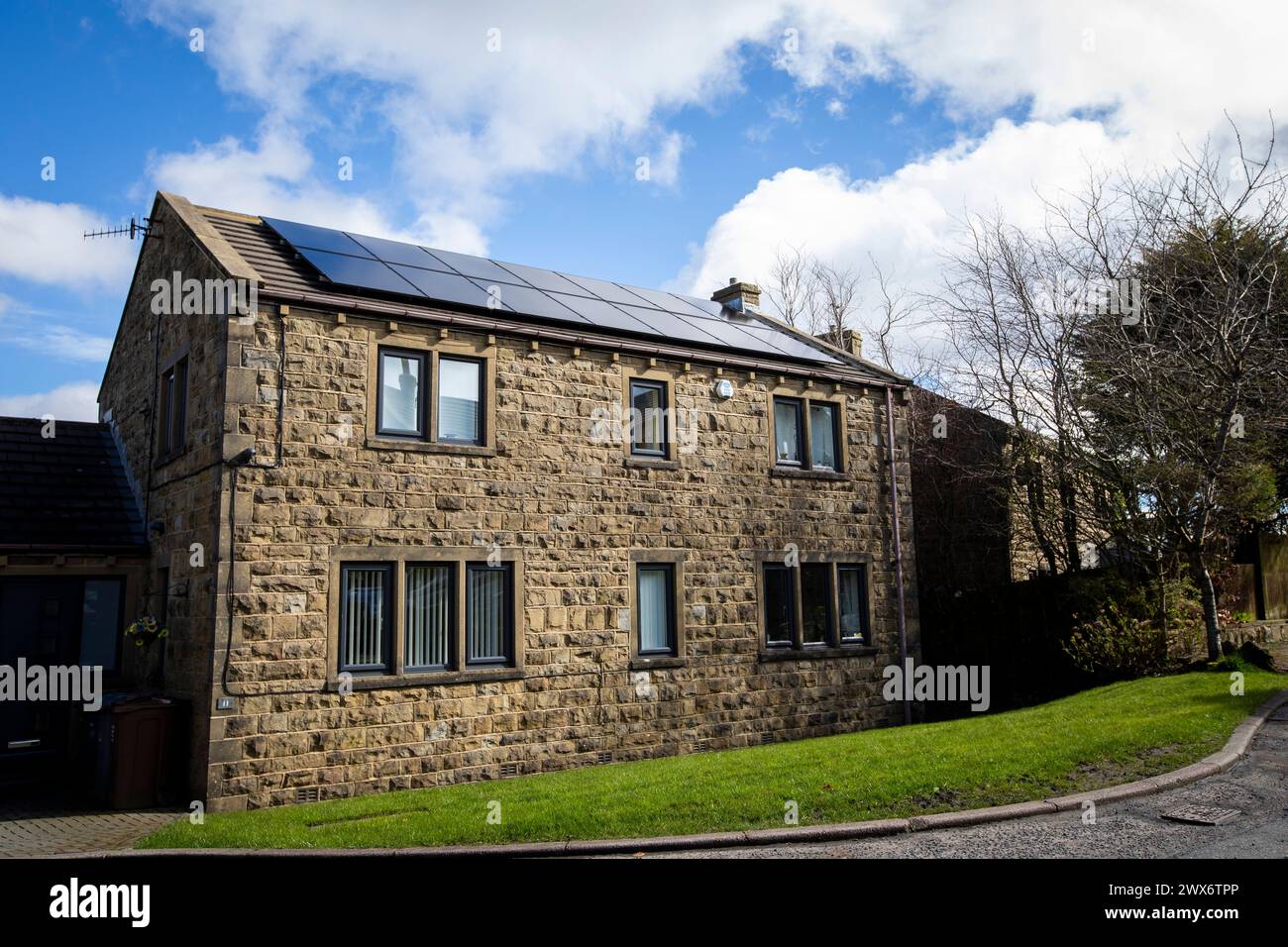 L'énergie solaire joue un rôle limité dans la production d'électricité au Royaume-Uni. Il y avait peu d'installations jusqu'en 2010, lorsque le gouvernement britannique a imposé des subventions sous la forme d'un tarif de rachat (FIT), payé par tous les consommateurs d'électricité. Au cours des années suivantes, le coût des panneaux photovoltaïques (PV) a baissé et les taux D'AJUSTEMENT pour les nouvelles installations ont été réduits progressivement jusqu'à ce que le régime ferme aux nouvelles applications en 2019. En 2023, plus de 14,4 gigawatts (GW) avaient été installés, dont un tiers solaire sur les toits. Maisons et maisons à Queensbury, West Yorkshire, Royaume-Uni avec des panneaux solaires par une journée ensoleillée. Banque D'Images