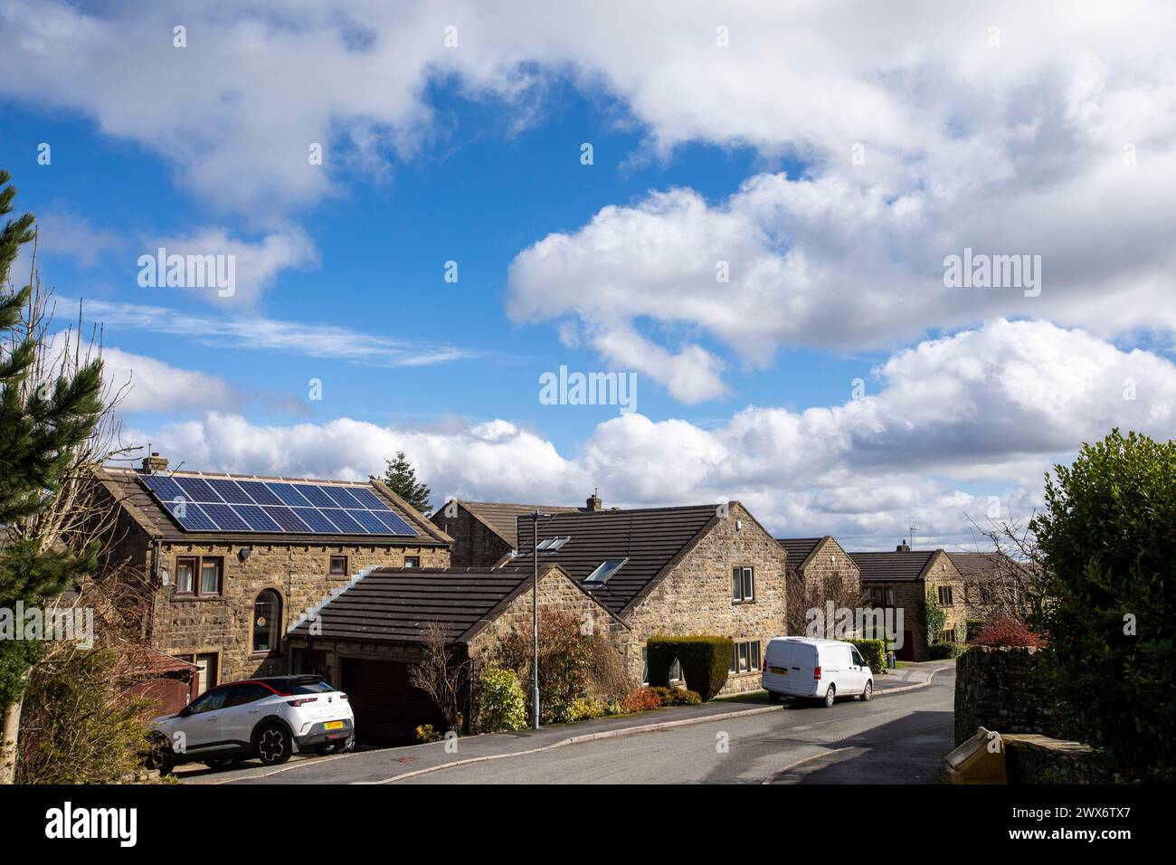 L'énergie solaire joue un rôle limité dans la production d'électricité au Royaume-Uni. Il y avait peu d'installations jusqu'en 2010, lorsque le gouvernement britannique a imposé des subventions sous la forme d'un tarif de rachat (FIT), payé par tous les consommateurs d'électricité. Au cours des années suivantes, le coût des panneaux photovoltaïques (PV) a baissé et les taux D'AJUSTEMENT pour les nouvelles installations ont été réduits progressivement jusqu'à ce que le régime ferme aux nouvelles applications en 2019. En 2023, plus de 14,4 gigawatts (GW) avaient été installés, dont un tiers solaire sur les toits. Maisons et maisons à Queensbury, West Yorkshire, Royaume-Uni avec des panneaux solaires par une journée ensoleillée. Banque D'Images