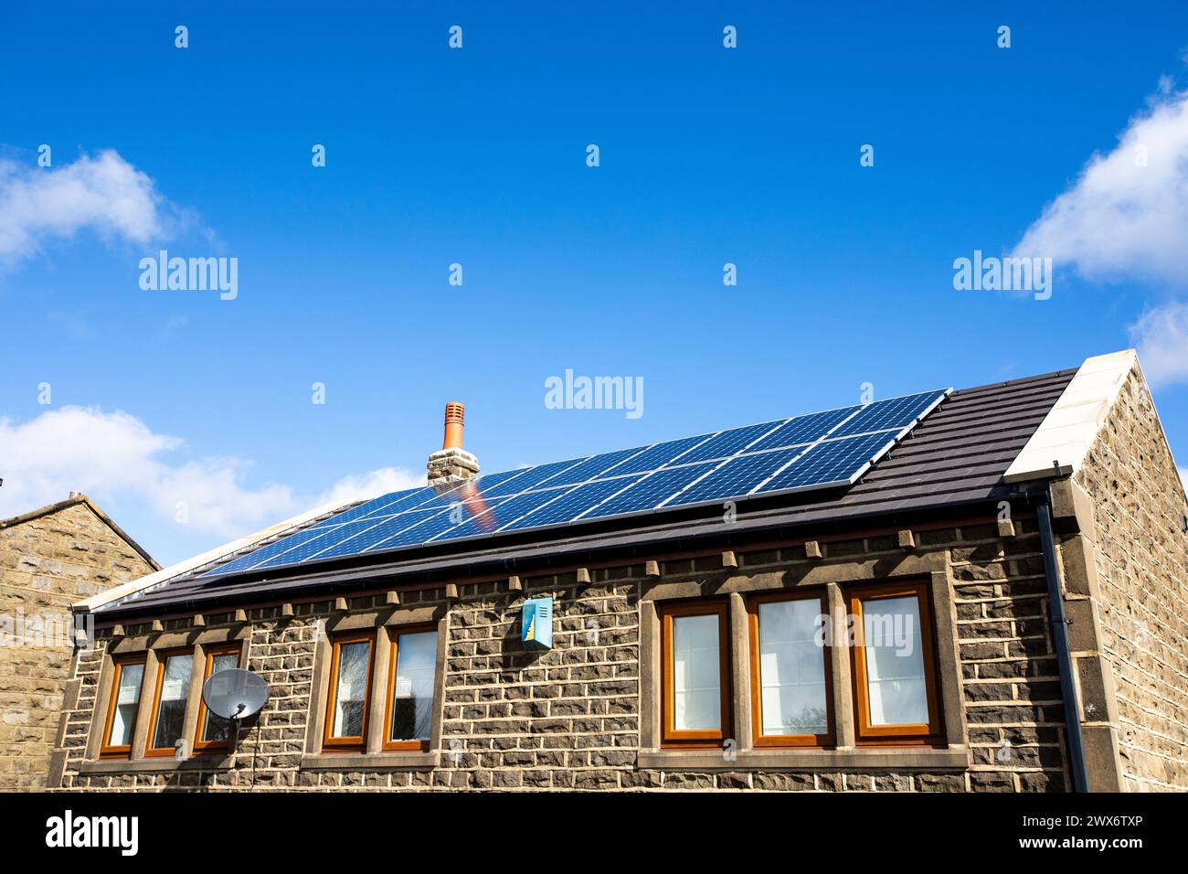 L'énergie solaire joue un rôle limité dans la production d'électricité au Royaume-Uni. Il y avait peu d'installations jusqu'en 2010, lorsque le gouvernement britannique a imposé des subventions sous la forme d'un tarif de rachat (FIT), payé par tous les consommateurs d'électricité. Au cours des années suivantes, le coût des panneaux photovoltaïques (PV) a baissé et les taux D'AJUSTEMENT pour les nouvelles installations ont été réduits progressivement jusqu'à ce que le régime ferme aux nouvelles applications en 2019. En 2023, plus de 14,4 gigawatts (GW) avaient été installés, dont un tiers solaire sur les toits. Maisons et maisons à Queensbury, West Yorkshire, Royaume-Uni avec des panneaux solaires par une journée ensoleillée. Banque D'Images
