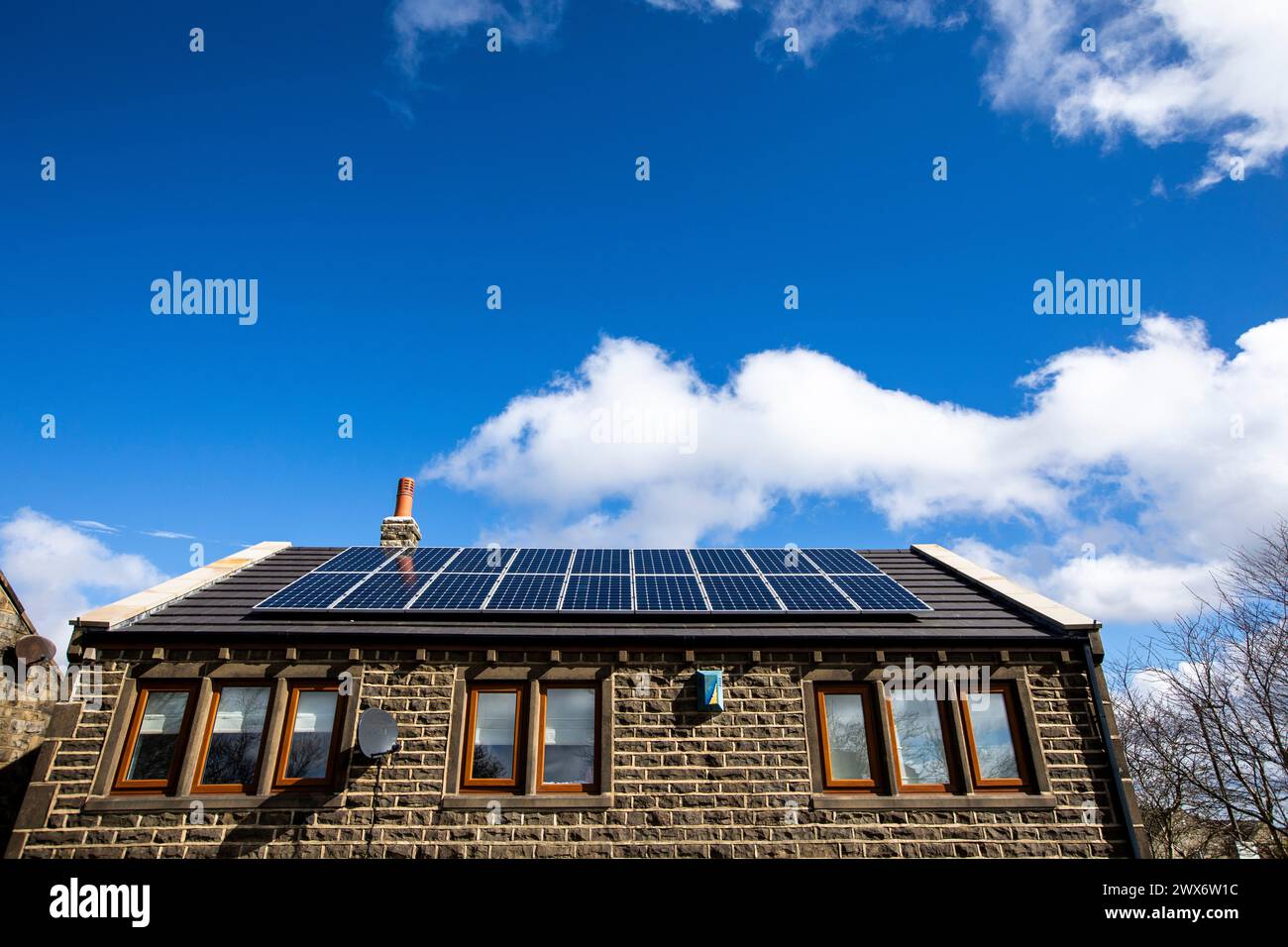 L'énergie solaire joue un rôle limité dans la production d'électricité au Royaume-Uni. Il y avait peu d'installations jusqu'en 2010, lorsque le gouvernement britannique a imposé des subventions sous la forme d'un tarif de rachat (FIT), payé par tous les consommateurs d'électricité. Au cours des années suivantes, le coût des panneaux photovoltaïques (PV) a baissé et les taux D'AJUSTEMENT pour les nouvelles installations ont été réduits progressivement jusqu'à ce que le régime ferme aux nouvelles applications en 2019. En 2023, plus de 14,4 gigawatts (GW) avaient été installés, dont un tiers solaire sur les toits. Maisons et maisons à Queensbury, West Yorkshire, Royaume-Uni avec des panneaux solaires par une journée ensoleillée. Banque D'Images