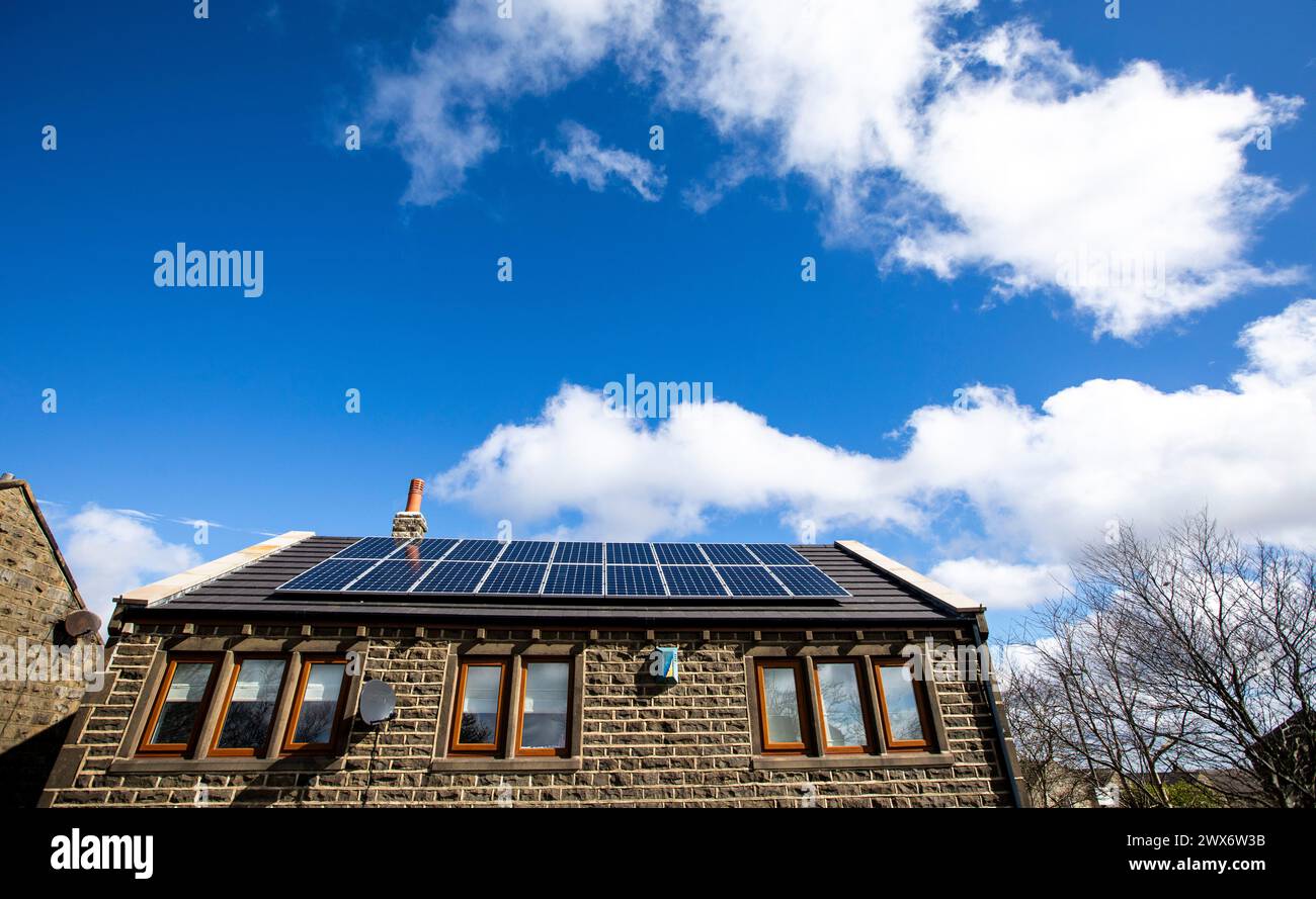L'énergie solaire joue un rôle limité dans la production d'électricité au Royaume-Uni. Il y avait peu d'installations jusqu'en 2010, lorsque le gouvernement britannique a imposé des subventions sous la forme d'un tarif de rachat (FIT), payé par tous les consommateurs d'électricité. Au cours des années suivantes, le coût des panneaux photovoltaïques (PV) a baissé et les taux D'AJUSTEMENT pour les nouvelles installations ont été réduits progressivement jusqu'à ce que le régime ferme aux nouvelles applications en 2019. En 2023, plus de 14,4 gigawatts (GW) avaient été installés, dont un tiers solaire sur les toits. Maisons et maisons à Queensbury, West Yorkshire, Royaume-Uni avec des panneaux solaires par une journée ensoleillée. Banque D'Images