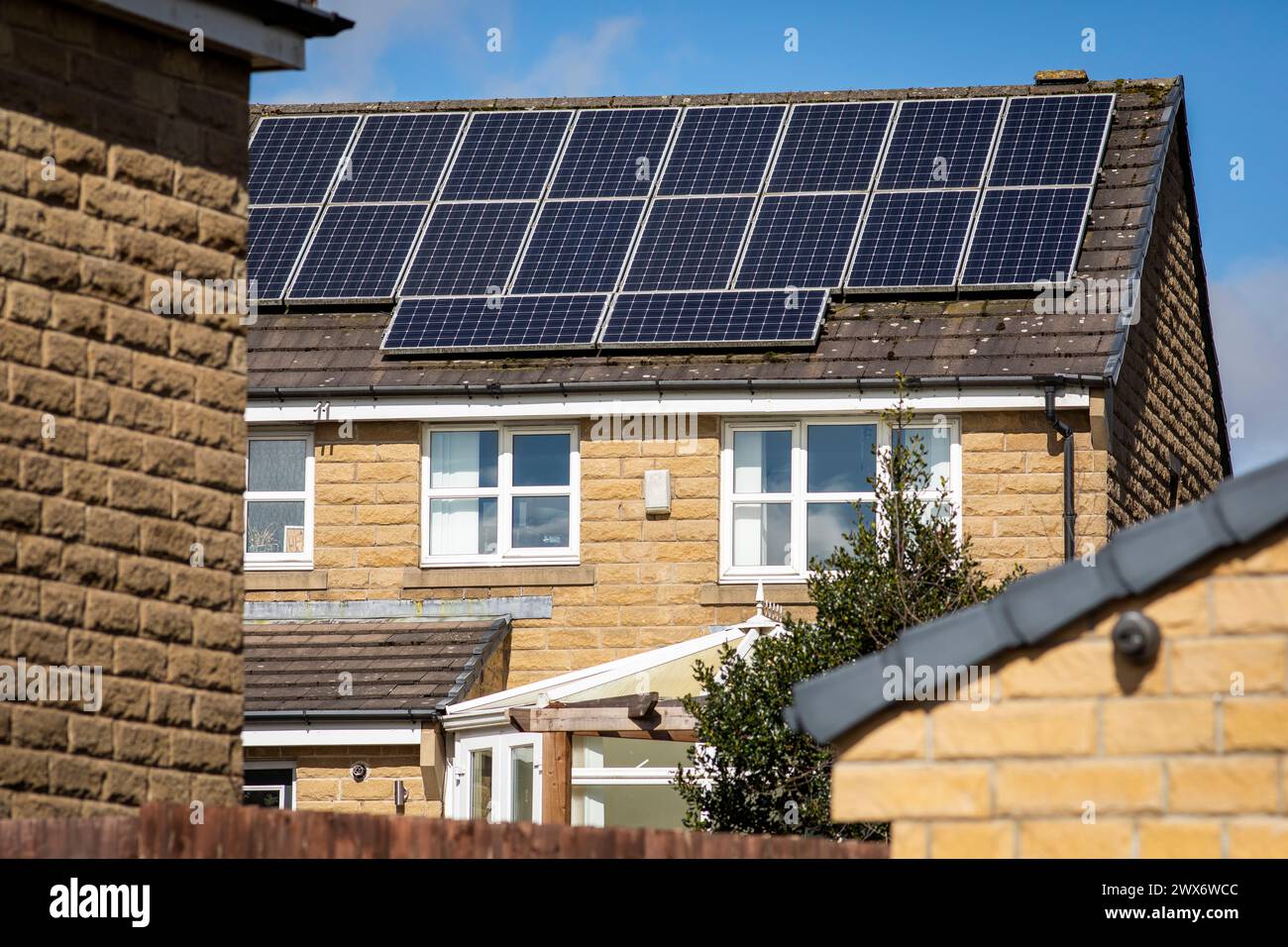 L'énergie solaire joue un rôle limité dans la production d'électricité au Royaume-Uni. Il y avait peu d'installations jusqu'en 2010, lorsque le gouvernement britannique a imposé des subventions sous la forme d'un tarif de rachat (FIT), payé par tous les consommateurs d'électricité. Au cours des années suivantes, le coût des panneaux photovoltaïques (PV) a baissé et les taux D'AJUSTEMENT pour les nouvelles installations ont été réduits progressivement jusqu'à ce que le régime ferme aux nouvelles applications en 2019. En 2023, plus de 14,4 gigawatts (GW) avaient été installés, dont un tiers solaire sur les toits. Maisons et maisons à Queensbury, West Yorkshire, Royaume-Uni avec des panneaux solaires par une journée ensoleillée. Banque D'Images