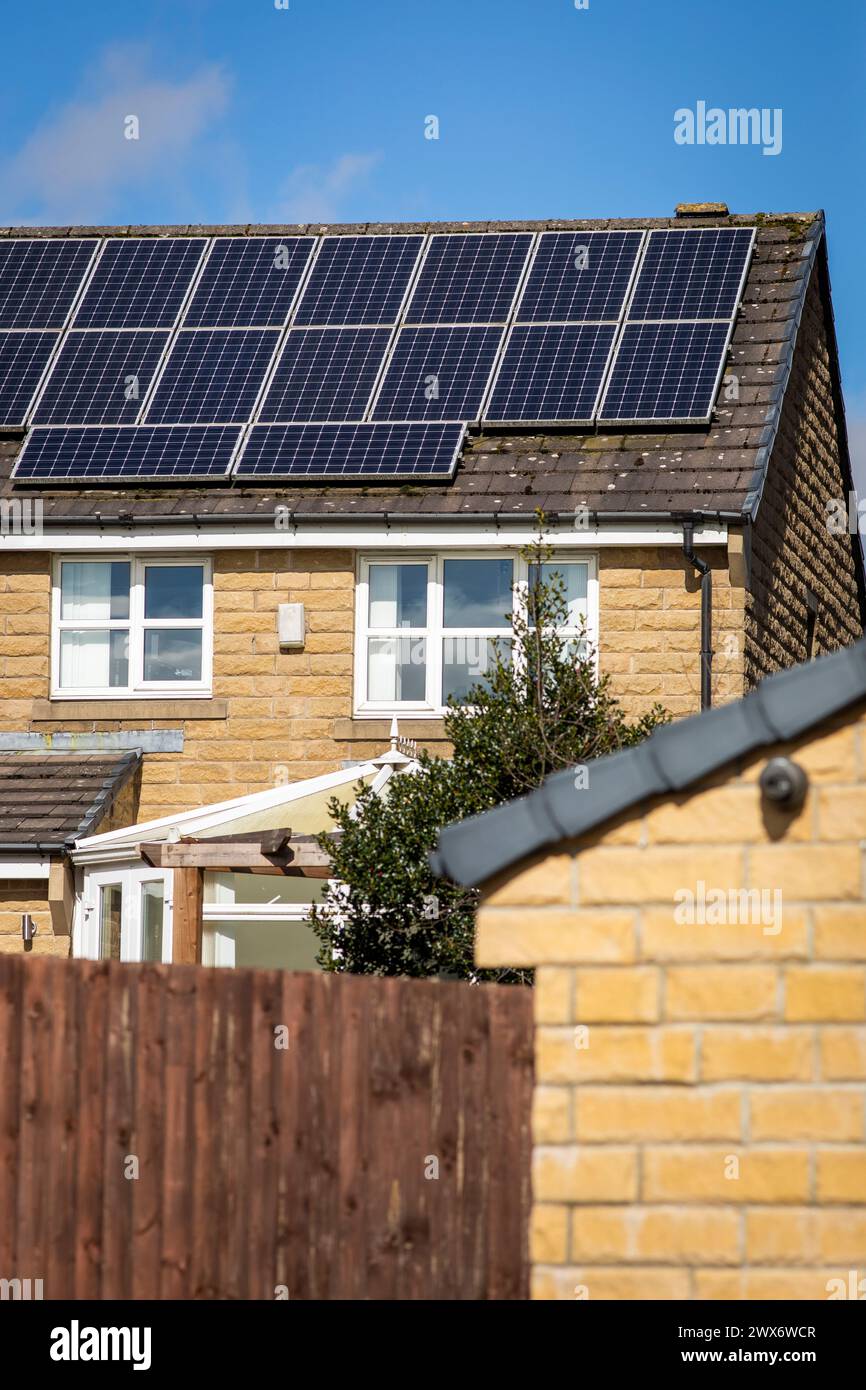 L'énergie solaire joue un rôle limité dans la production d'électricité au Royaume-Uni. Il y avait peu d'installations jusqu'en 2010, lorsque le gouvernement britannique a imposé des subventions sous la forme d'un tarif de rachat (FIT), payé par tous les consommateurs d'électricité. Au cours des années suivantes, le coût des panneaux photovoltaïques (PV) a baissé et les taux D'AJUSTEMENT pour les nouvelles installations ont été réduits progressivement jusqu'à ce que le régime ferme aux nouvelles applications en 2019. En 2023, plus de 14,4 gigawatts (GW) avaient été installés, dont un tiers solaire sur les toits. Maisons et maisons à Queensbury, West Yorkshire, Royaume-Uni avec des panneaux solaires par une journée ensoleillée. Banque D'Images