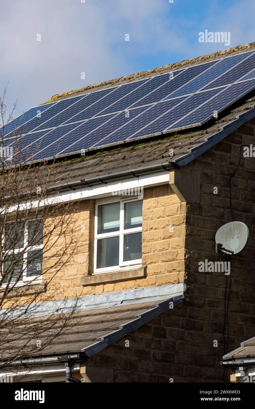 L'énergie solaire joue un rôle limité dans la production d'électricité au Royaume-Uni. Il y avait peu d'installations jusqu'en 2010, lorsque le gouvernement britannique a imposé des subventions sous la forme d'un tarif de rachat (FIT), payé par tous les consommateurs d'électricité. Au cours des années suivantes, le coût des panneaux photovoltaïques (PV) a baissé et les taux D'AJUSTEMENT pour les nouvelles installations ont été réduits progressivement jusqu'à ce que le régime ferme aux nouvelles applications en 2019. En 2023, plus de 14,4 gigawatts (GW) avaient été installés, dont un tiers solaire sur les toits. Maisons et maisons à Queensbury, West Yorkshire, Royaume-Uni avec des panneaux solaires par une journée ensoleillée. Banque D'Images