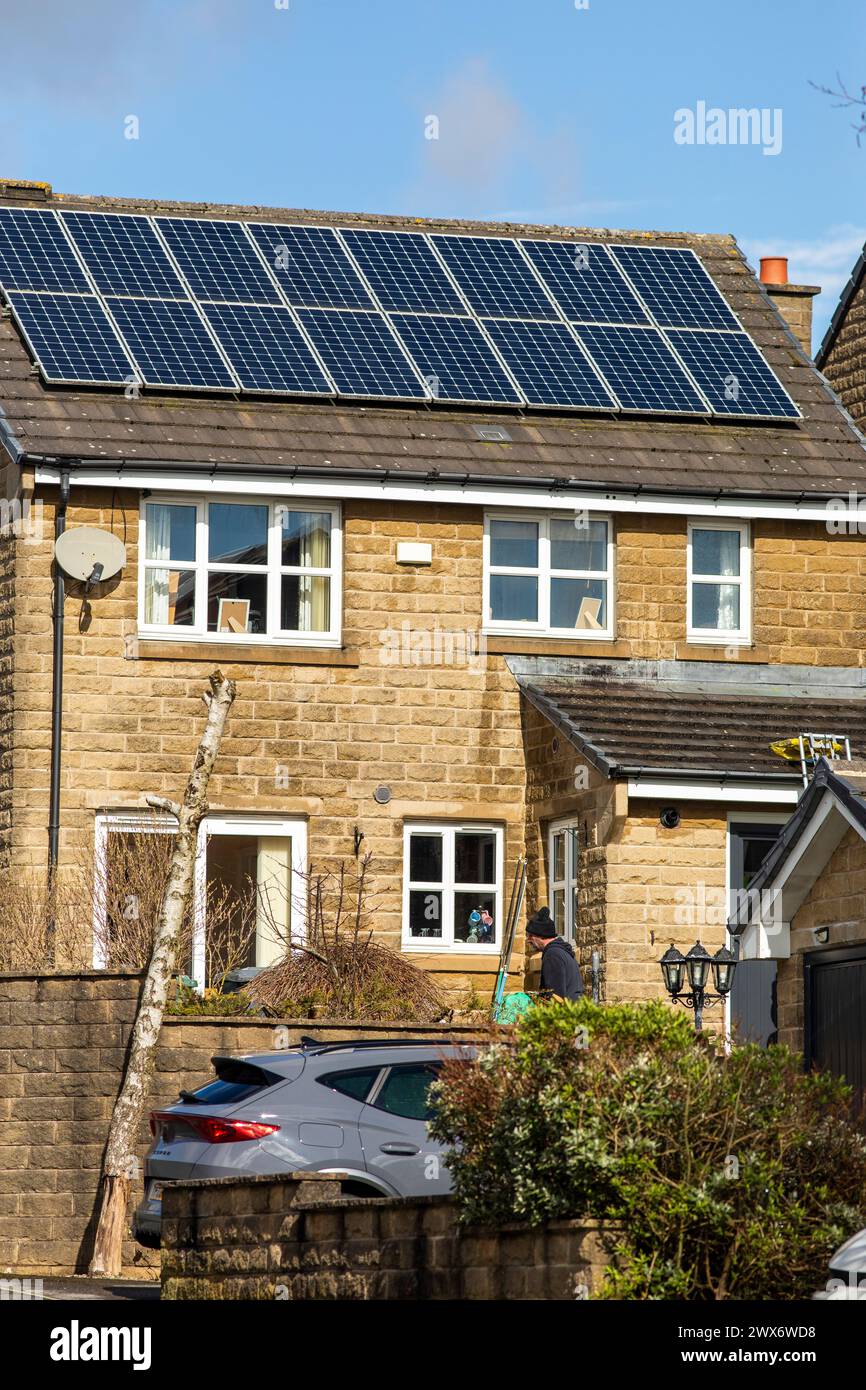 L'énergie solaire joue un rôle limité dans la production d'électricité au Royaume-Uni. Il y avait peu d'installations jusqu'en 2010, lorsque le gouvernement britannique a imposé des subventions sous la forme d'un tarif de rachat (FIT), payé par tous les consommateurs d'électricité. Au cours des années suivantes, le coût des panneaux photovoltaïques (PV) a baissé et les taux D'AJUSTEMENT pour les nouvelles installations ont été réduits progressivement jusqu'à ce que le régime ferme aux nouvelles applications en 2019. En 2023, plus de 14,4 gigawatts (GW) avaient été installés, dont un tiers solaire sur les toits. Maisons et maisons à Queensbury, West Yorkshire, Royaume-Uni avec des panneaux solaires par une journée ensoleillée. Banque D'Images