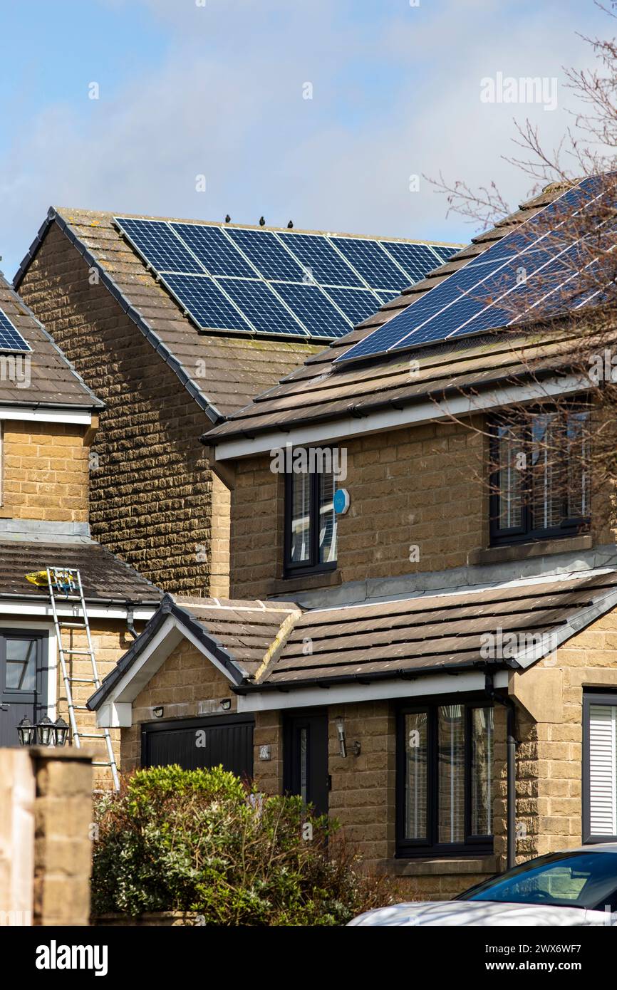 L'énergie solaire joue un rôle limité dans la production d'électricité au Royaume-Uni. Il y avait peu d'installations jusqu'en 2010, lorsque le gouvernement britannique a imposé des subventions sous la forme d'un tarif de rachat (FIT), payé par tous les consommateurs d'électricité. Au cours des années suivantes, le coût des panneaux photovoltaïques (PV) a baissé et les taux D'AJUSTEMENT pour les nouvelles installations ont été réduits progressivement jusqu'à ce que le régime ferme aux nouvelles applications en 2019. En 2023, plus de 14,4 gigawatts (GW) avaient été installés, dont un tiers solaire sur les toits. Maisons et maisons à Queensbury, West Yorkshire, Royaume-Uni avec des panneaux solaires par une journée ensoleillée. Banque D'Images