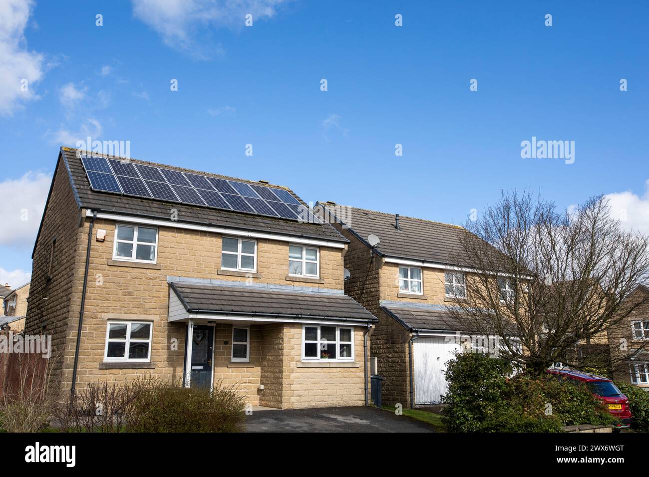L'énergie solaire joue un rôle limité dans la production d'électricité au Royaume-Uni. Il y avait peu d'installations jusqu'en 2010, lorsque le gouvernement britannique a imposé des subventions sous la forme d'un tarif de rachat (FIT), payé par tous les consommateurs d'électricité. Au cours des années suivantes, le coût des panneaux photovoltaïques (PV) a baissé et les taux D'AJUSTEMENT pour les nouvelles installations ont été réduits progressivement jusqu'à ce que le régime ferme aux nouvelles applications en 2019. En 2023, plus de 14,4 gigawatts (GW) avaient été installés, dont un tiers solaire sur les toits. Maisons et maisons à Queensbury, West Yorkshire, Royaume-Uni avec des panneaux solaires par une journée ensoleillée. Banque D'Images