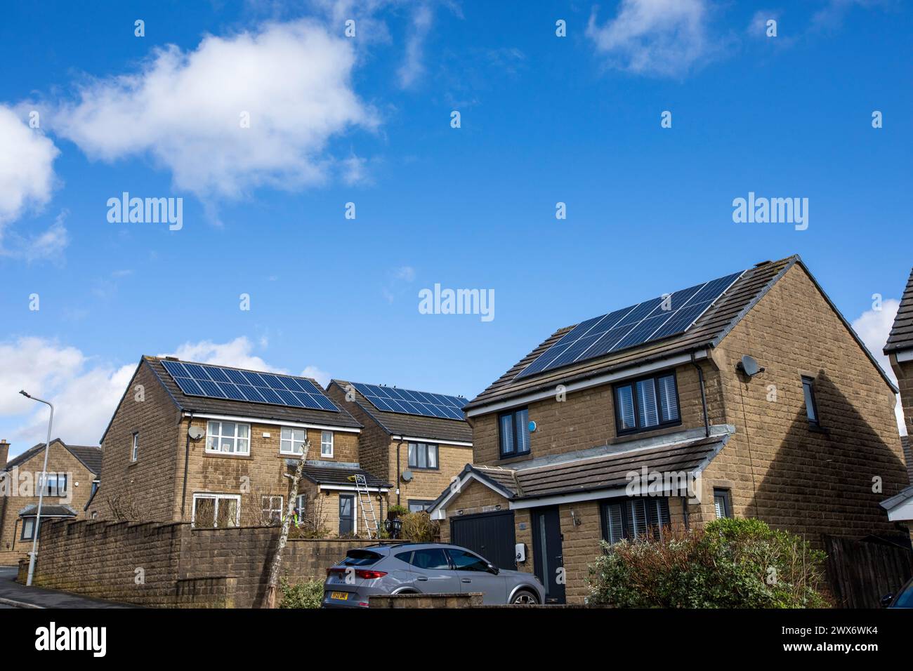 L'énergie solaire joue un rôle limité dans la production d'électricité au Royaume-Uni. Il y avait peu d'installations jusqu'en 2010, lorsque le gouvernement britannique a imposé des subventions sous la forme d'un tarif de rachat (FIT), payé par tous les consommateurs d'électricité. Au cours des années suivantes, le coût des panneaux photovoltaïques (PV) a baissé et les taux D'AJUSTEMENT pour les nouvelles installations ont été réduits progressivement jusqu'à ce que le régime ferme aux nouvelles applications en 2019. En 2023, plus de 14,4 gigawatts (GW) avaient été installés, dont un tiers solaire sur les toits. Maisons et maisons à Queensbury, West Yorkshire, Royaume-Uni avec des panneaux solaires par une journée ensoleillée. Banque D'Images