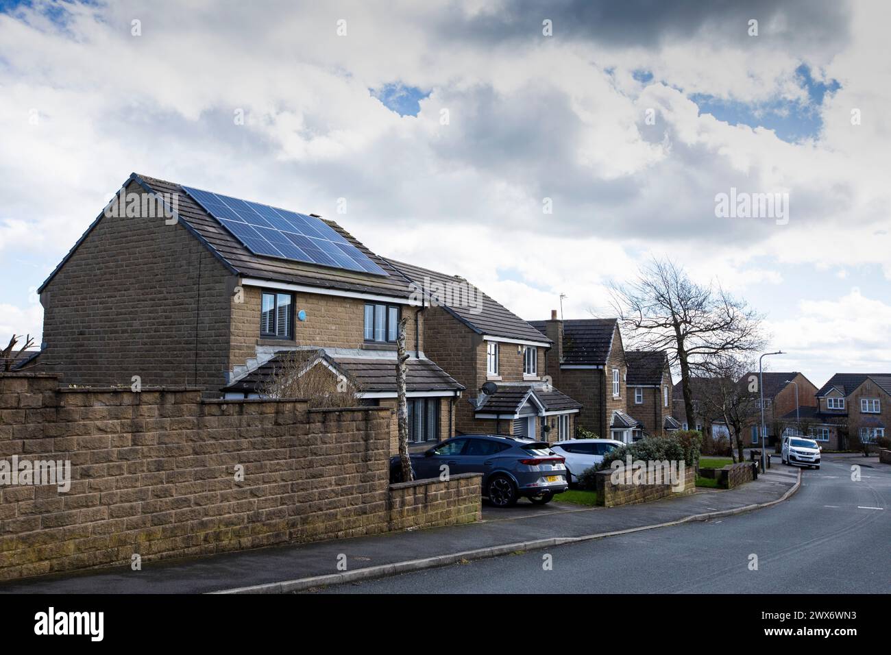 L'énergie solaire joue un rôle limité dans la production d'électricité au Royaume-Uni. Il y avait peu d'installations jusqu'en 2010, lorsque le gouvernement britannique a imposé des subventions sous la forme d'un tarif de rachat (FIT), payé par tous les consommateurs d'électricité. Au cours des années suivantes, le coût des panneaux photovoltaïques (PV) a baissé et les taux D'AJUSTEMENT pour les nouvelles installations ont été réduits progressivement jusqu'à ce que le régime ferme aux nouvelles applications en 2019. En 2023, plus de 14,4 gigawatts (GW) avaient été installés, dont un tiers solaire sur les toits. Maisons et maisons à Queensbury, West Yorkshire, Royaume-Uni avec des panneaux solaires par une journée ensoleillée. Banque D'Images