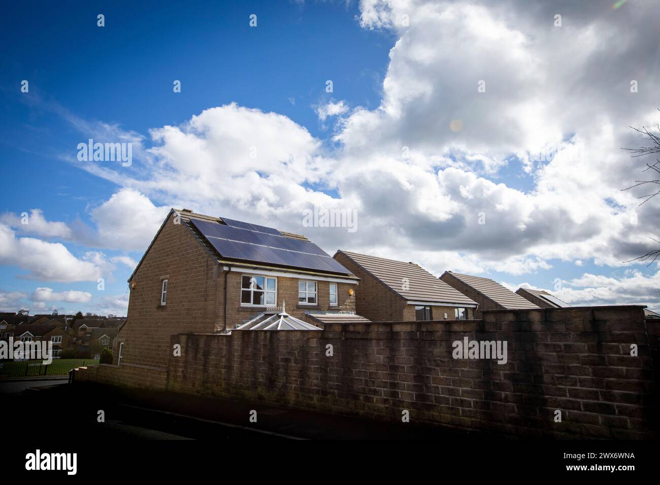L'énergie solaire joue un rôle limité dans la production d'électricité au Royaume-Uni. Il y avait peu d'installations jusqu'en 2010, lorsque le gouvernement britannique a imposé des subventions sous la forme d'un tarif de rachat (FIT), payé par tous les consommateurs d'électricité. Au cours des années suivantes, le coût des panneaux photovoltaïques (PV) a baissé et les taux D'AJUSTEMENT pour les nouvelles installations ont été réduits progressivement jusqu'à ce que le régime ferme aux nouvelles applications en 2019. En 2023, plus de 14,4 gigawatts (GW) avaient été installés, dont un tiers solaire sur les toits. Maisons et maisons à Queensbury, West Yorkshire, Royaume-Uni avec des panneaux solaires par une journée ensoleillée. Banque D'Images