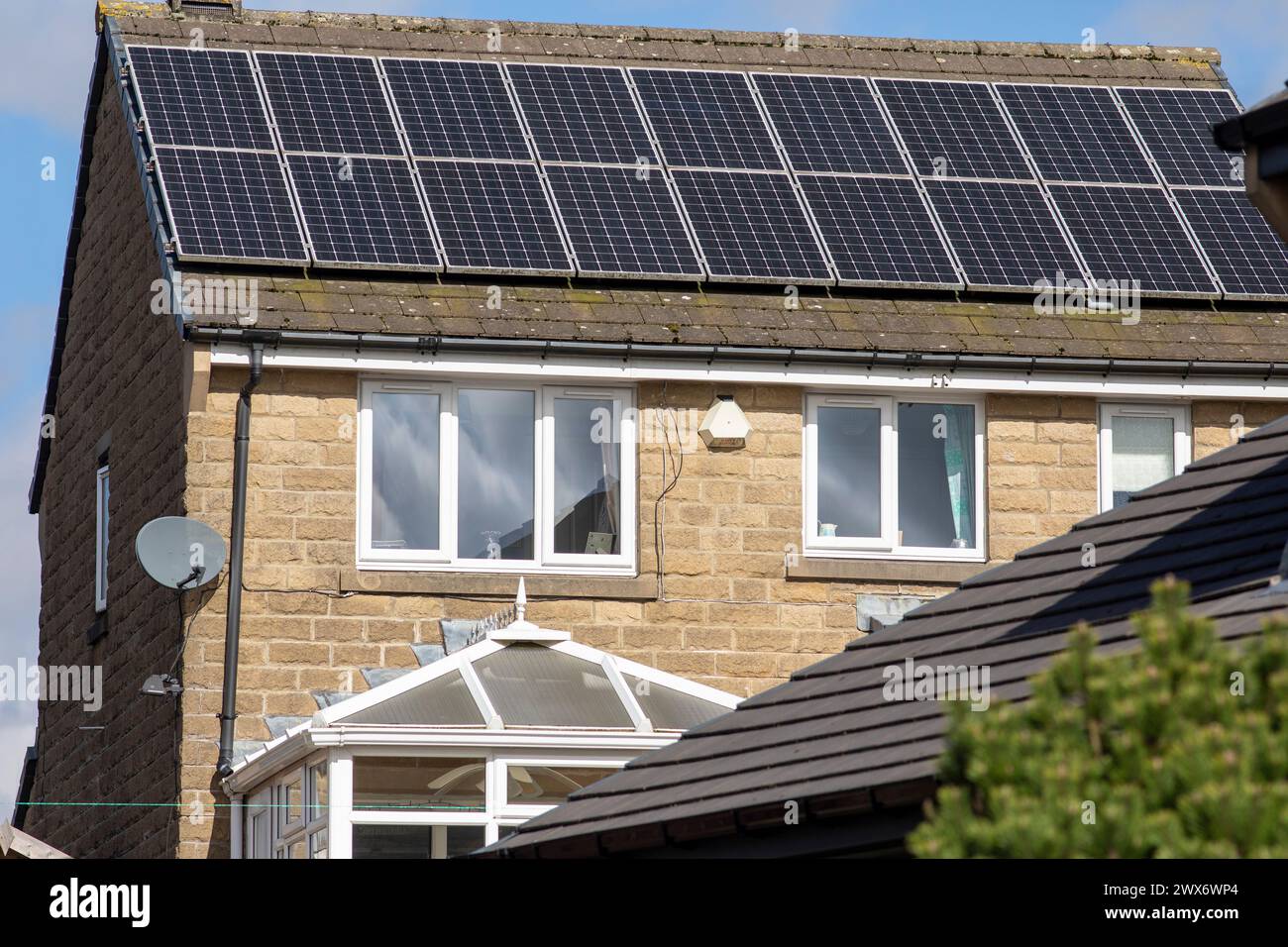 L'énergie solaire joue un rôle limité dans la production d'électricité au Royaume-Uni. Il y avait peu d'installations jusqu'en 2010, lorsque le gouvernement britannique a imposé des subventions sous la forme d'un tarif de rachat (FIT), payé par tous les consommateurs d'électricité. Au cours des années suivantes, le coût des panneaux photovoltaïques (PV) a baissé et les taux D'AJUSTEMENT pour les nouvelles installations ont été réduits progressivement jusqu'à ce que le régime ferme aux nouvelles applications en 2019. En 2023, plus de 14,4 gigawatts (GW) avaient été installés, dont un tiers solaire sur les toits. Maisons et maisons à Queensbury, West Yorkshire, Royaume-Uni avec des panneaux solaires par une journée ensoleillée. Banque D'Images