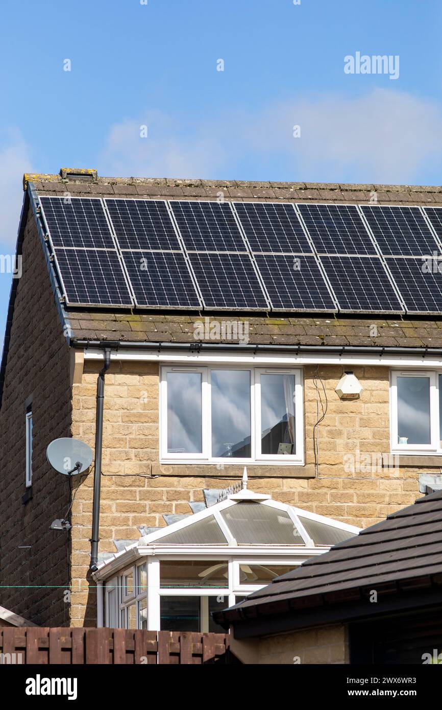 L'énergie solaire joue un rôle limité dans la production d'électricité au Royaume-Uni. Il y avait peu d'installations jusqu'en 2010, lorsque le gouvernement britannique a imposé des subventions sous la forme d'un tarif de rachat (FIT), payé par tous les consommateurs d'électricité. Au cours des années suivantes, le coût des panneaux photovoltaïques (PV) a baissé et les taux D'AJUSTEMENT pour les nouvelles installations ont été réduits progressivement jusqu'à ce que le régime ferme aux nouvelles applications en 2019. En 2023, plus de 14,4 gigawatts (GW) avaient été installés, dont un tiers solaire sur les toits. Maisons et maisons à Queensbury, West Yorkshire, Royaume-Uni avec des panneaux solaires par une journée ensoleillée. Banque D'Images
