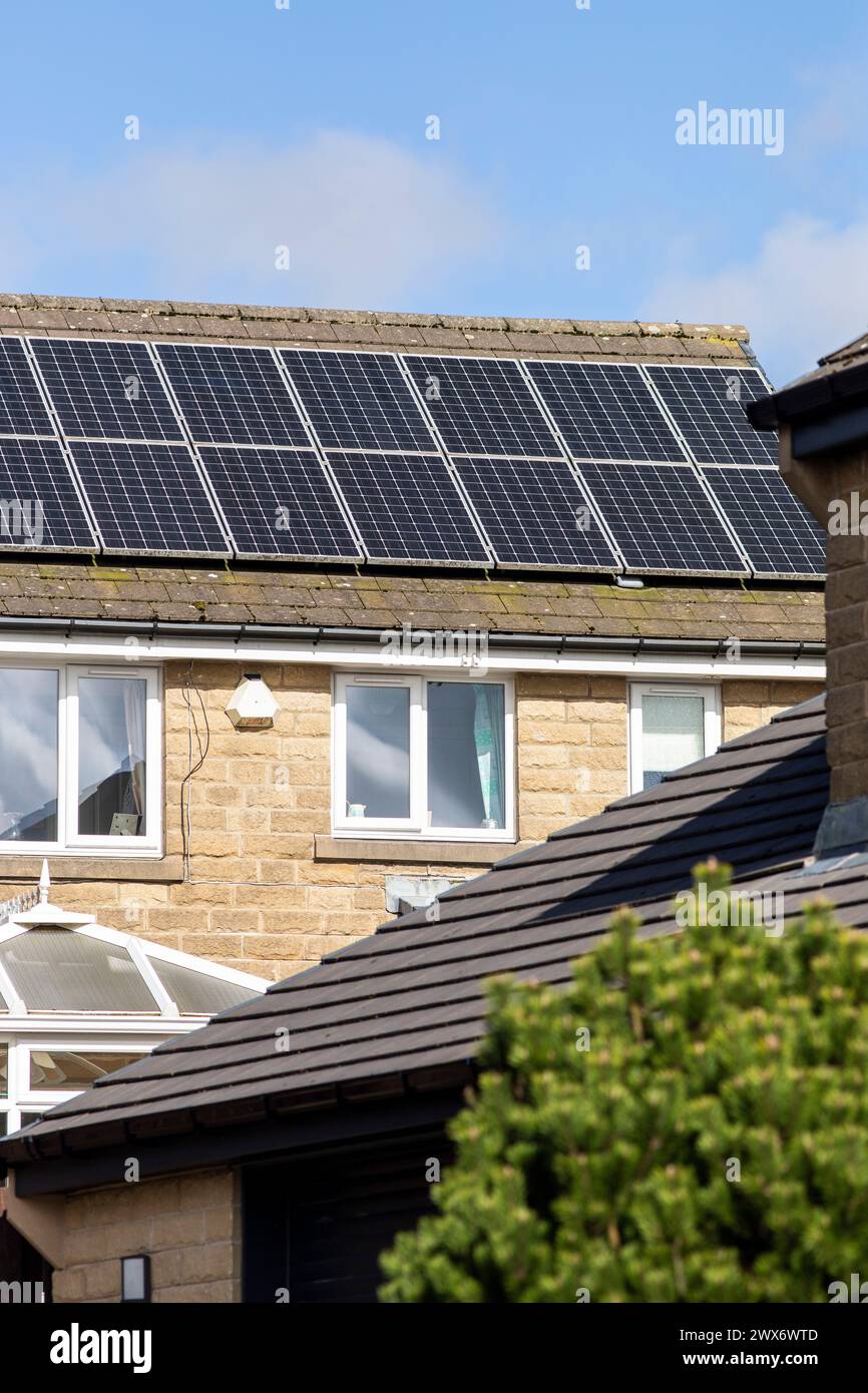 L'énergie solaire joue un rôle limité dans la production d'électricité au Royaume-Uni. Il y avait peu d'installations jusqu'en 2010, lorsque le gouvernement britannique a imposé des subventions sous la forme d'un tarif de rachat (FIT), payé par tous les consommateurs d'électricité. Au cours des années suivantes, le coût des panneaux photovoltaïques (PV) a baissé et les taux D'AJUSTEMENT pour les nouvelles installations ont été réduits progressivement jusqu'à ce que le régime ferme aux nouvelles applications en 2019. En 2023, plus de 14,4 gigawatts (GW) avaient été installés, dont un tiers solaire sur les toits. Maisons et maisons à Queensbury, West Yorkshire, Royaume-Uni avec des panneaux solaires par une journée ensoleillée. Banque D'Images