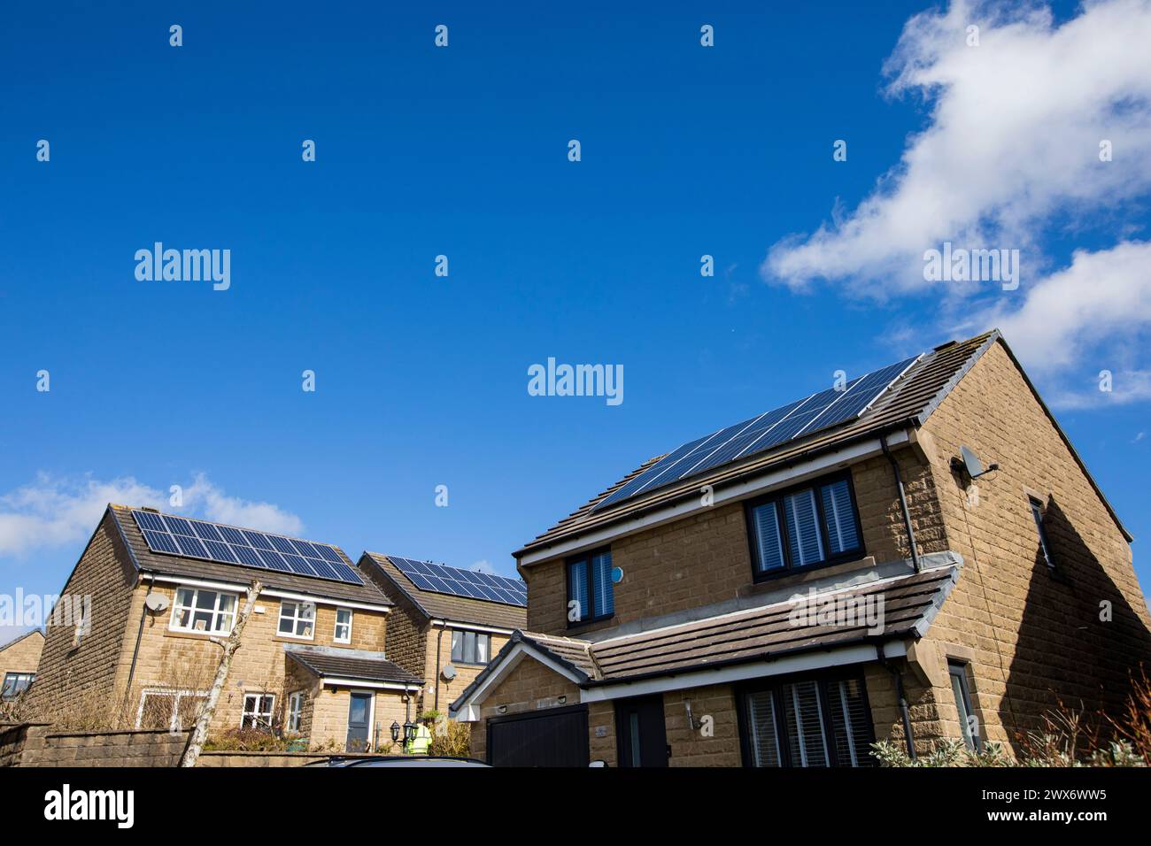 L'énergie solaire joue un rôle limité dans la production d'électricité au Royaume-Uni. Il y avait peu d'installations jusqu'en 2010, lorsque le gouvernement britannique a imposé des subventions sous la forme d'un tarif de rachat (FIT), payé par tous les consommateurs d'électricité. Au cours des années suivantes, le coût des panneaux photovoltaïques (PV) a baissé et les taux D'AJUSTEMENT pour les nouvelles installations ont été réduits progressivement jusqu'à ce que le régime ferme aux nouvelles applications en 2019. En 2023, plus de 14,4 gigawatts (GW) avaient été installés, dont un tiers solaire sur les toits. Maisons et maisons à Queensbury, West Yorkshire, Royaume-Uni avec des panneaux solaires par une journée ensoleillée. Banque D'Images