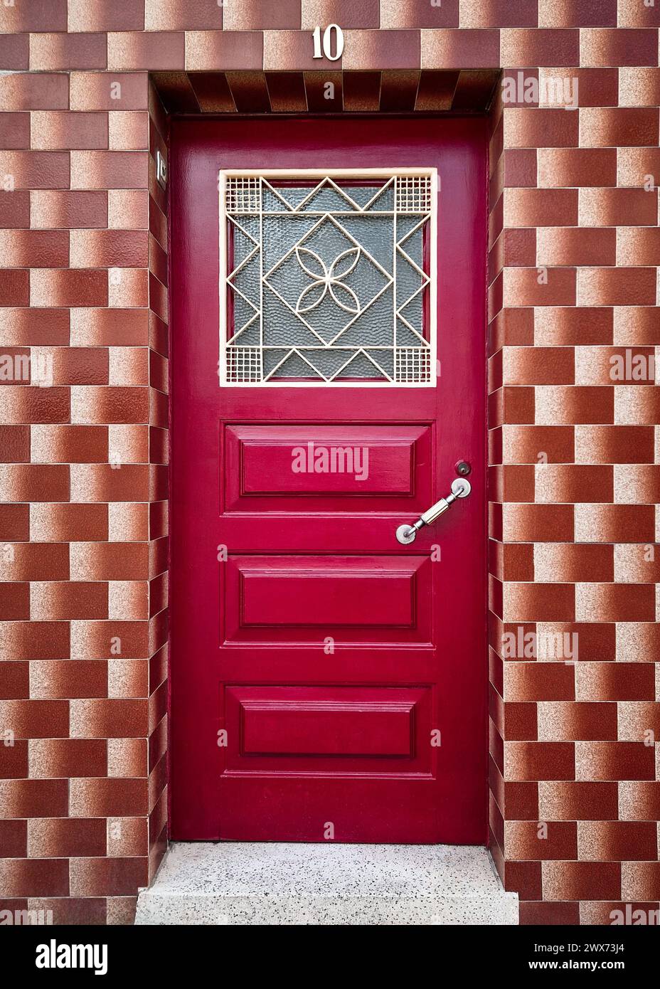 Façade d'une vieille maison restaurée avec des carreaux bruns vintage sur les murs et une porte en bois peinte dans une couleur rouge vif avec trappe décorative en métal Banque D'Images