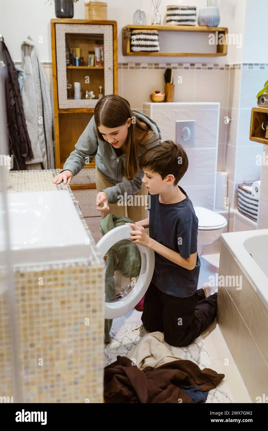 Sœur adolescente aidant frère tout en faisant la lessive dans la salle de bain à la maison Banque D'Images