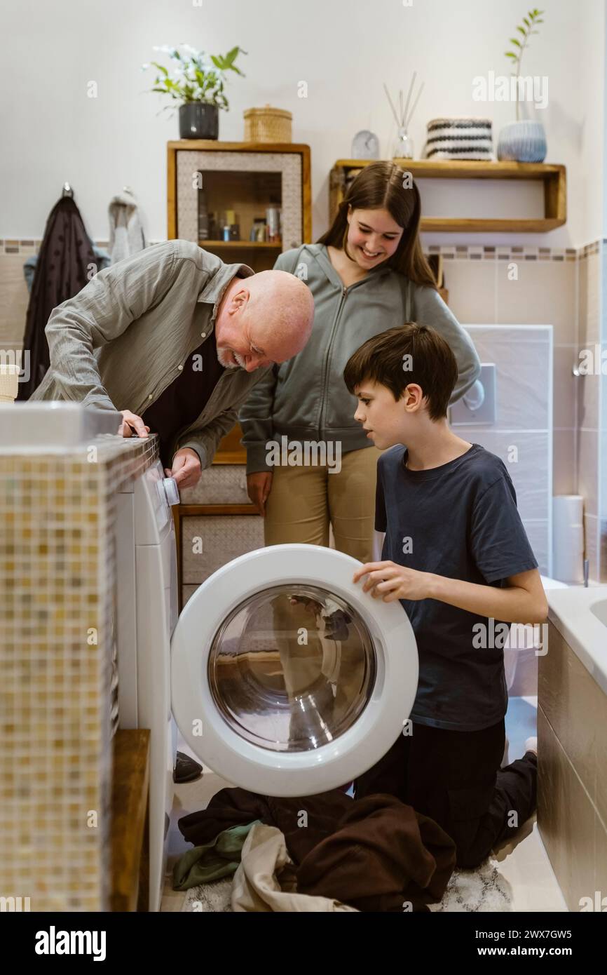 Homme senior aidant les petits-enfants tout en faisant la lessive dans la salle de bain à la maison Banque D'Images