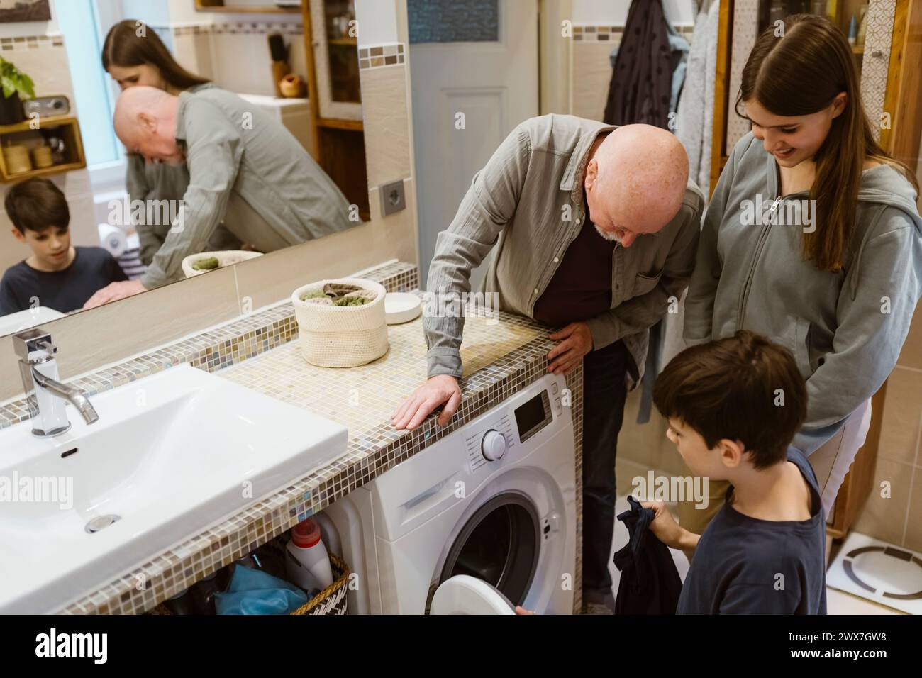 Homme senior enseignant aux petits-enfants à utiliser la machine à laver dans la salle de bain à la maison Banque D'Images