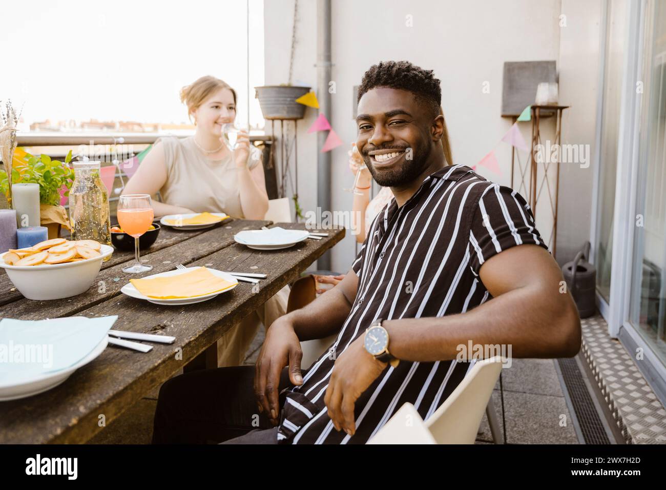 Portrait de jeune homme souriant assis avec des amis à la table à manger dans le balcon Banque D'Images