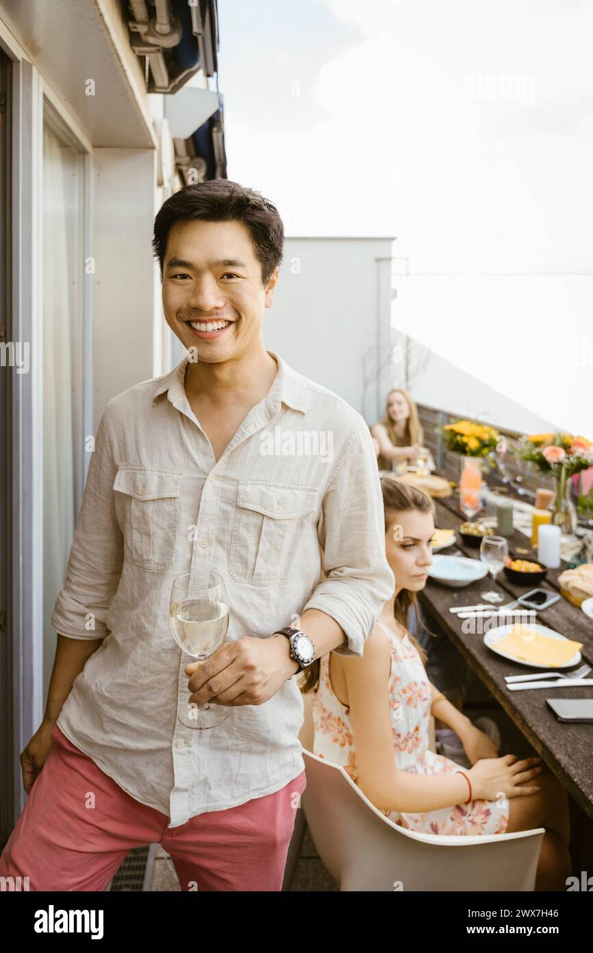 Portrait d'homme souriant tenant du verre de vin tout en se tenant debout dans le balcon Banque D'Images