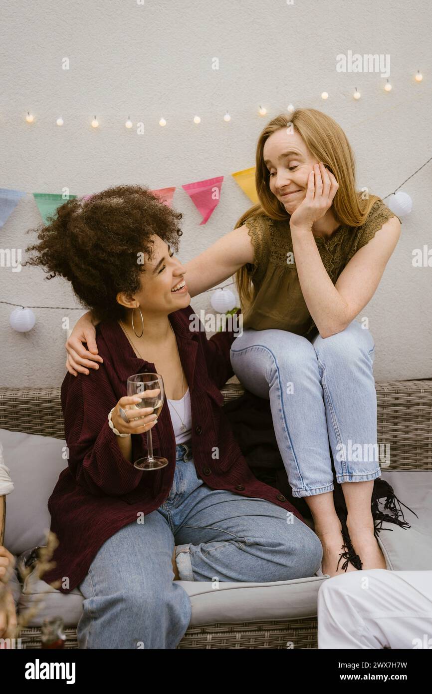 Femme souriante assise avec une amie tenant du verre de vin à la fête sur le balcon Banque D'Images