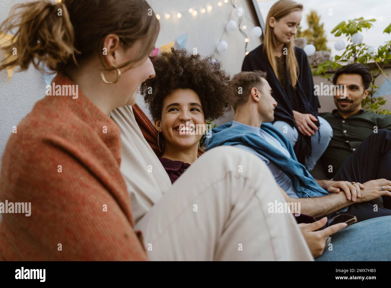 Femme souriante parlant avec des amies féminines tout en étant assis à la fête dans le balcon Banque D'Images