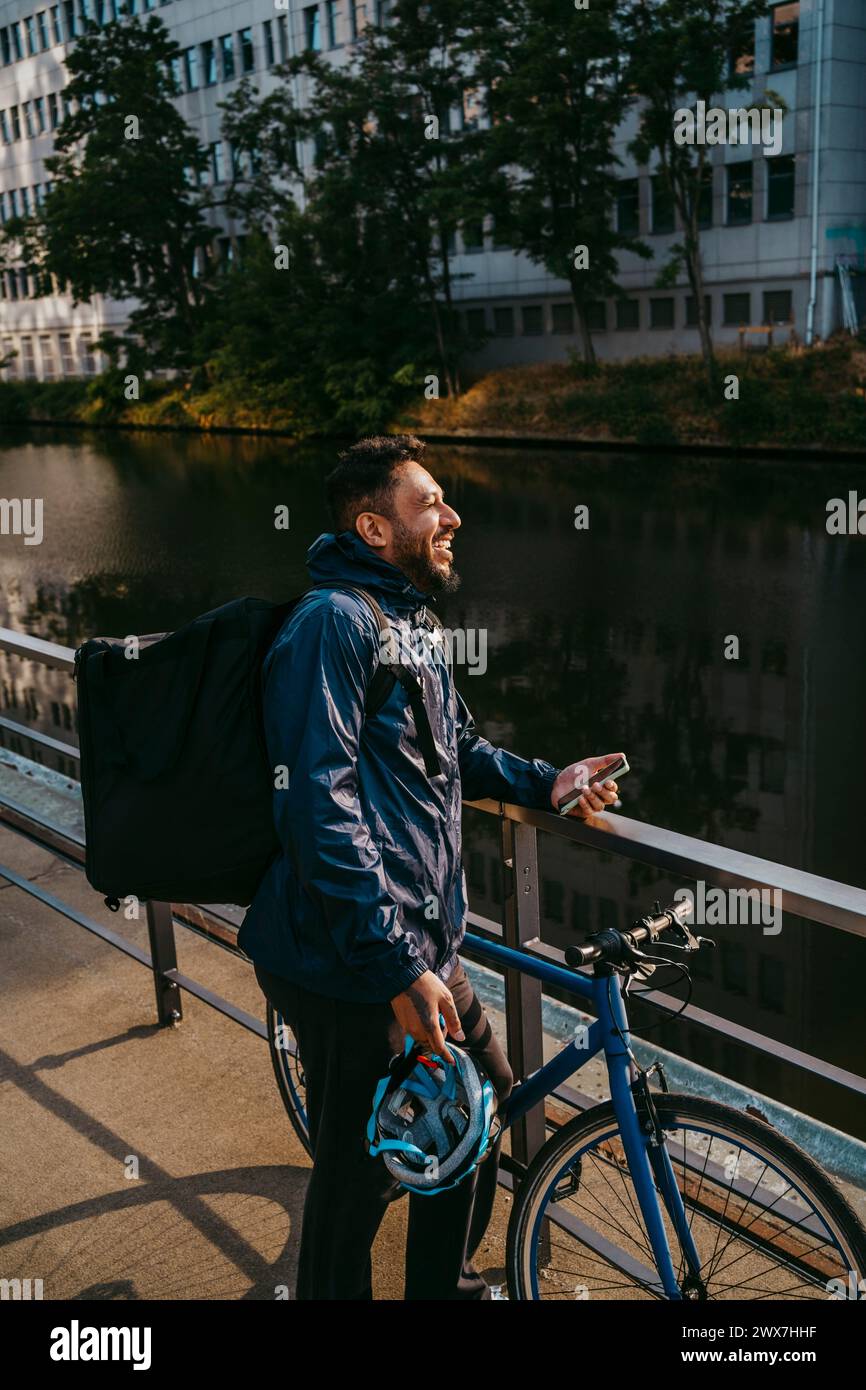 Souriant homme livrant de la nourriture debout près de la rampe avec une bicyclette Banque D'Images