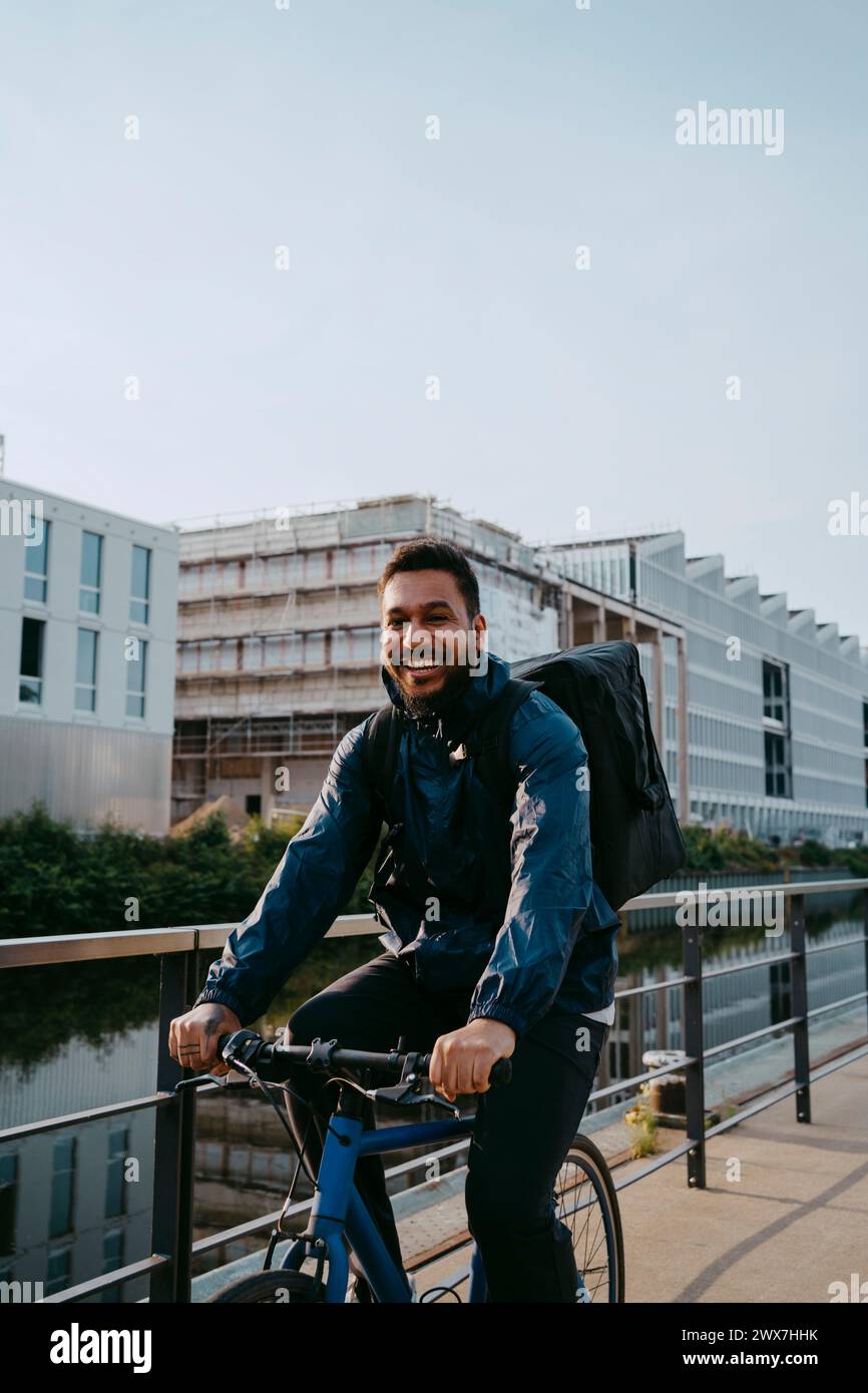 Portrait de jeune livreur masculin souriant cycliste sur un sentier pédestre en ville Banque D'Images