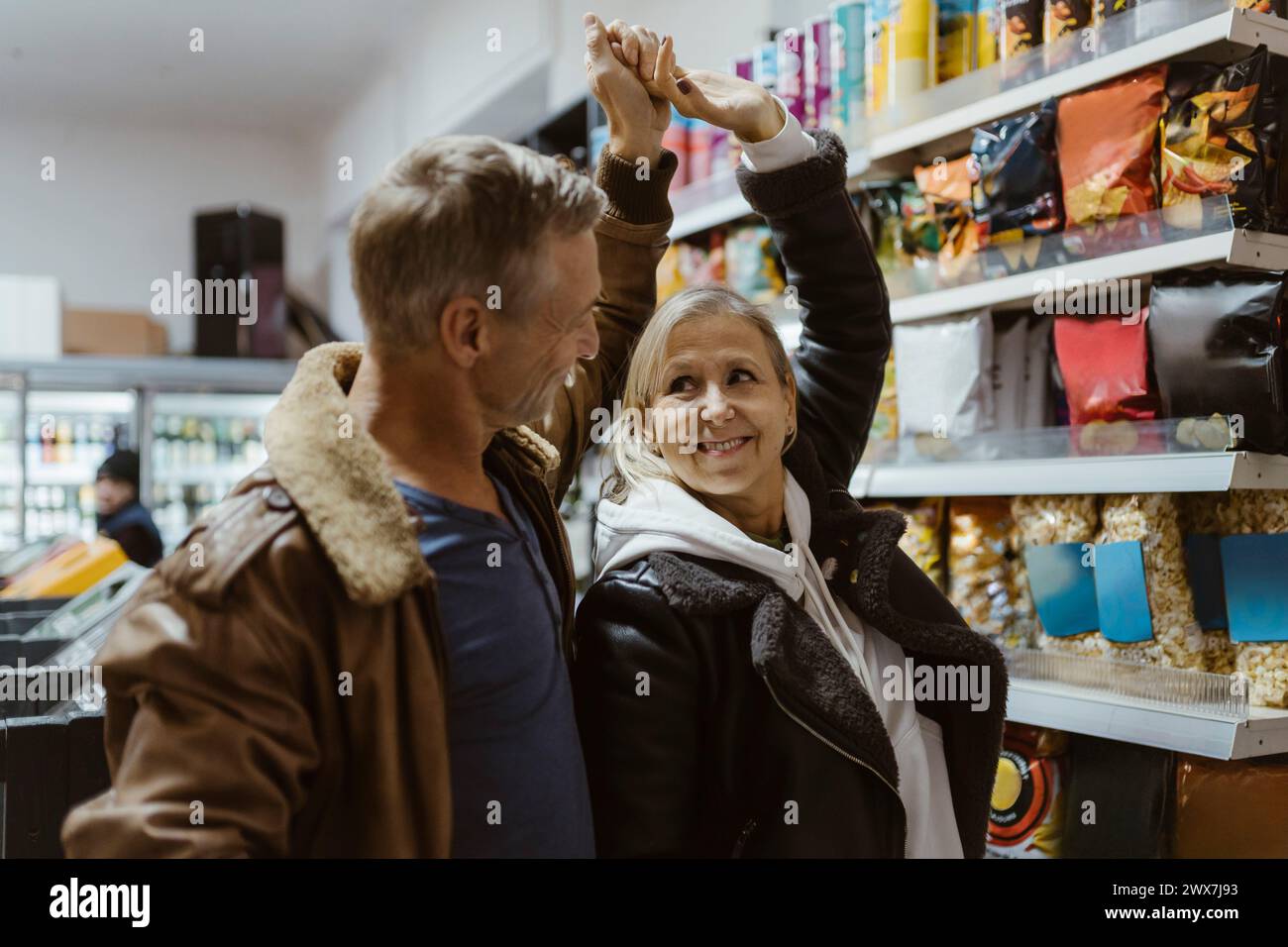 Heureux couple mûr dansant ensemble avec la main levée lors du shopping au supermarché Banque D'Images