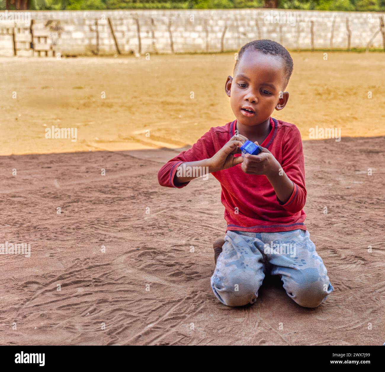 enfant africain jouant avec une voiture jouet dans le sable dans la cour, vie de village africain Banque D'Images