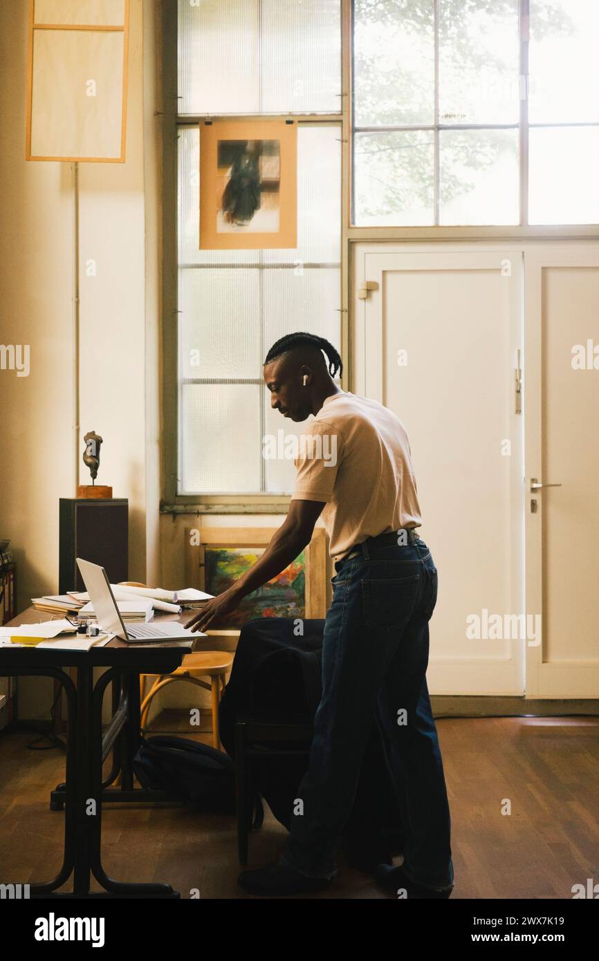 Vue latérale de l'entrepreneur masculin utilisant un ordinateur portable tout en se tenant dans le bureau à domicile Banque D'Images