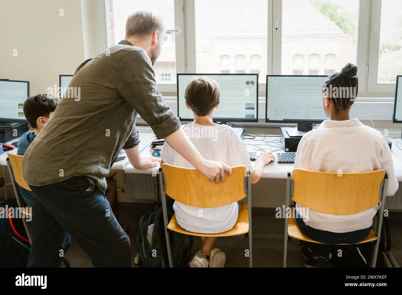 Enseignant masculin aidant les élèves à surfer sur Internet à travers des ordinateurs en classe à l'école Banque D'Images