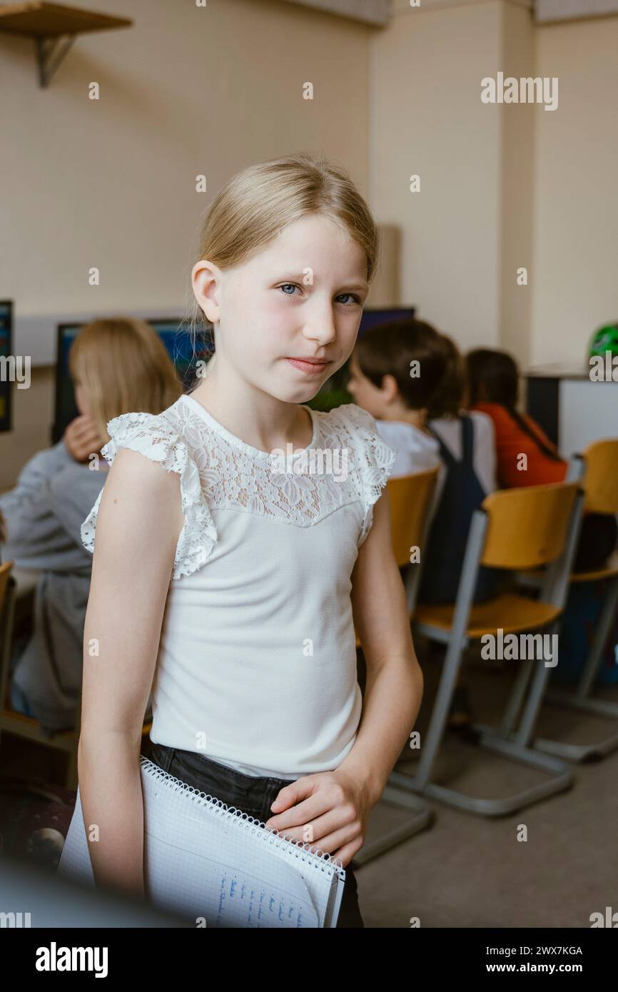 Portrait d'une fille tenant un cahier tout en se tenant debout dans une salle de classe informatique à l'école Banque D'Images