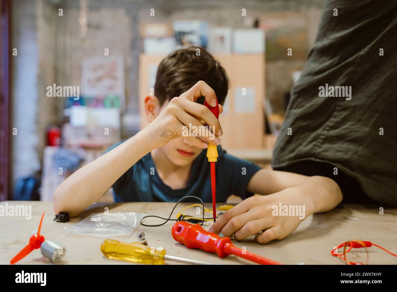 Garçon apprenant à réparer un composant électrique à l'aide d'un tournevis à l'atelier à l'école Banque D'Images