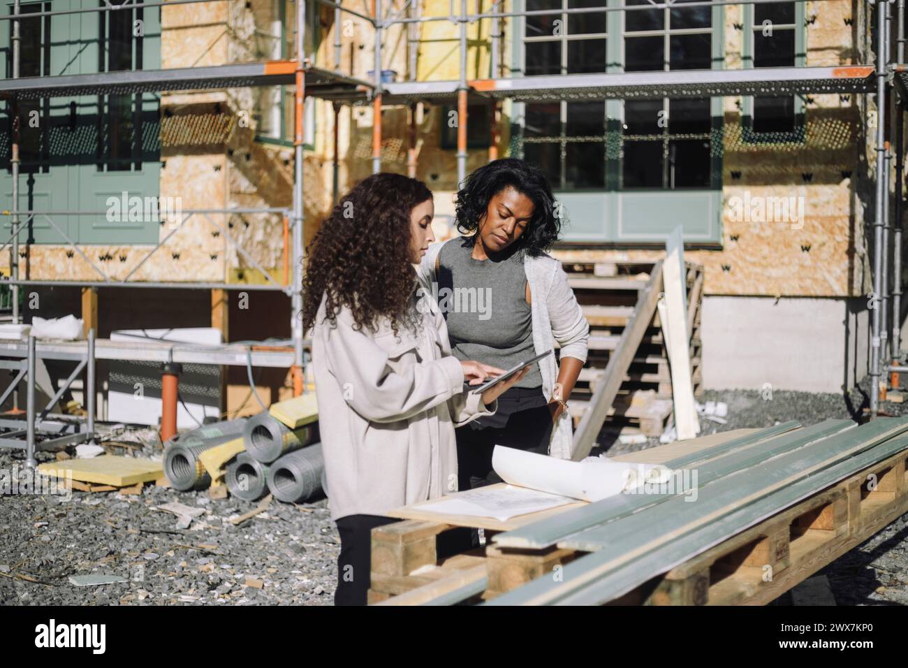 Femme ingénieur de construction discutant avec le client sur la table numérique tout en se tenant devant l'apa en construction Banque D'Images