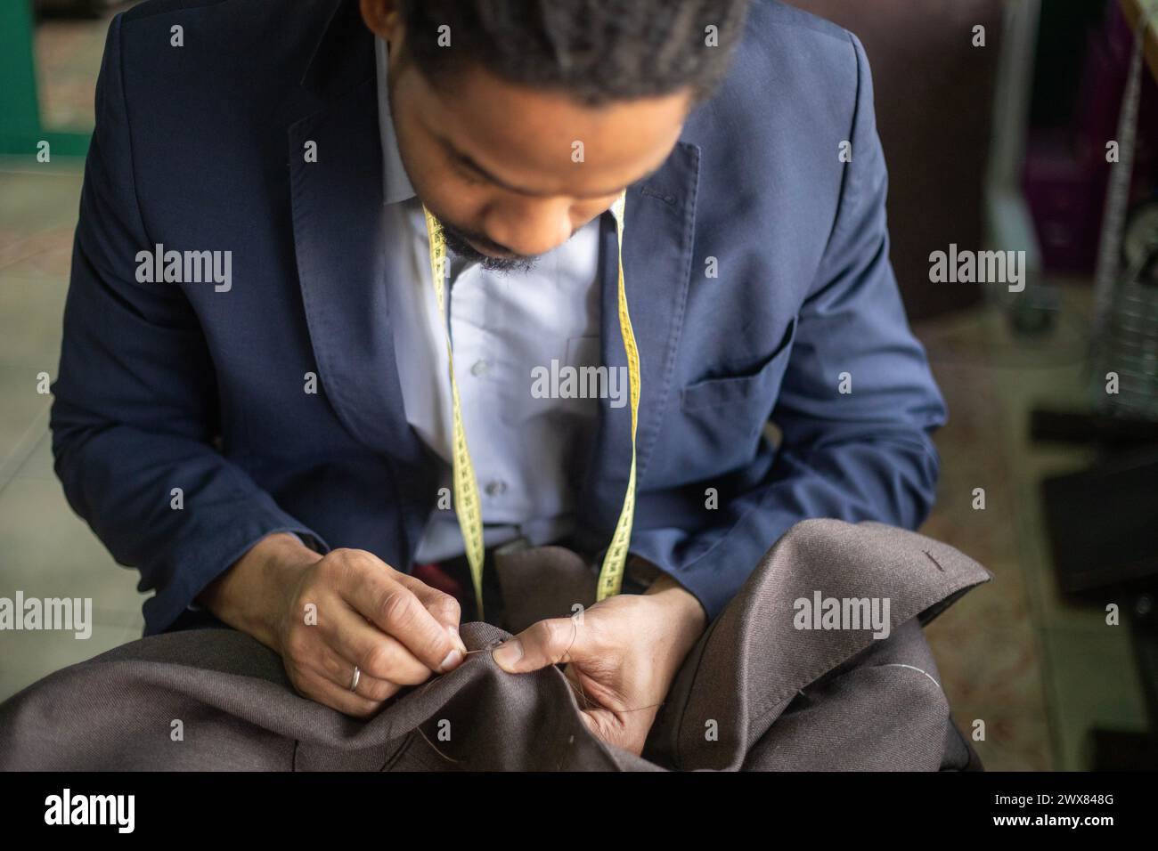 Gros plan détaillé d'un jeune tailleur afro-américain cousant à la main la boutonnière d'une veste sur mesure tout en étant super concentré sur le travail Banque D'Images