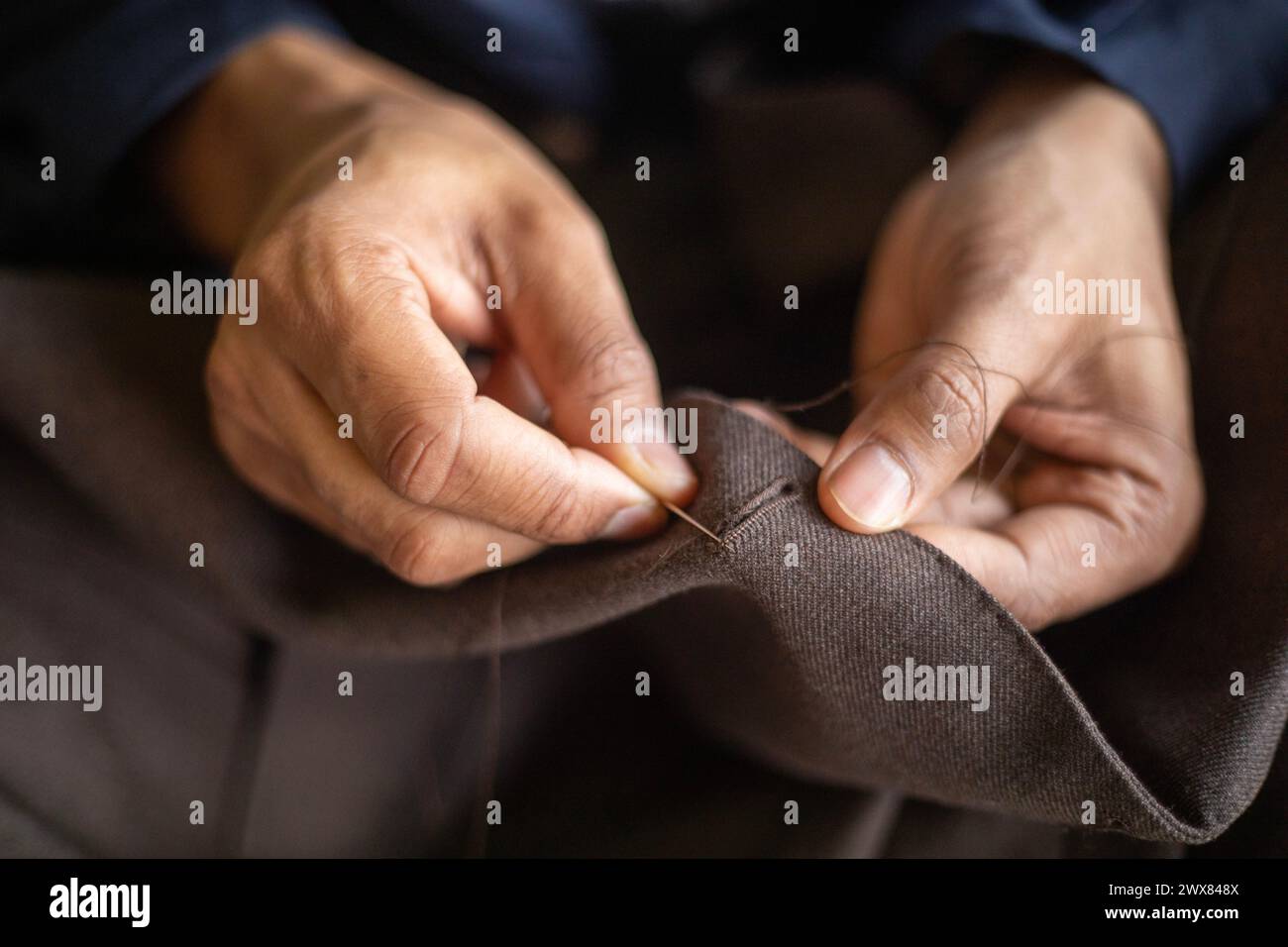 Gros plan détaillé d'un jeune tailleur afro-américain cousant à la main la boutonnière d'une veste sur mesure tout en étant super concentré sur le travail Banque D'Images